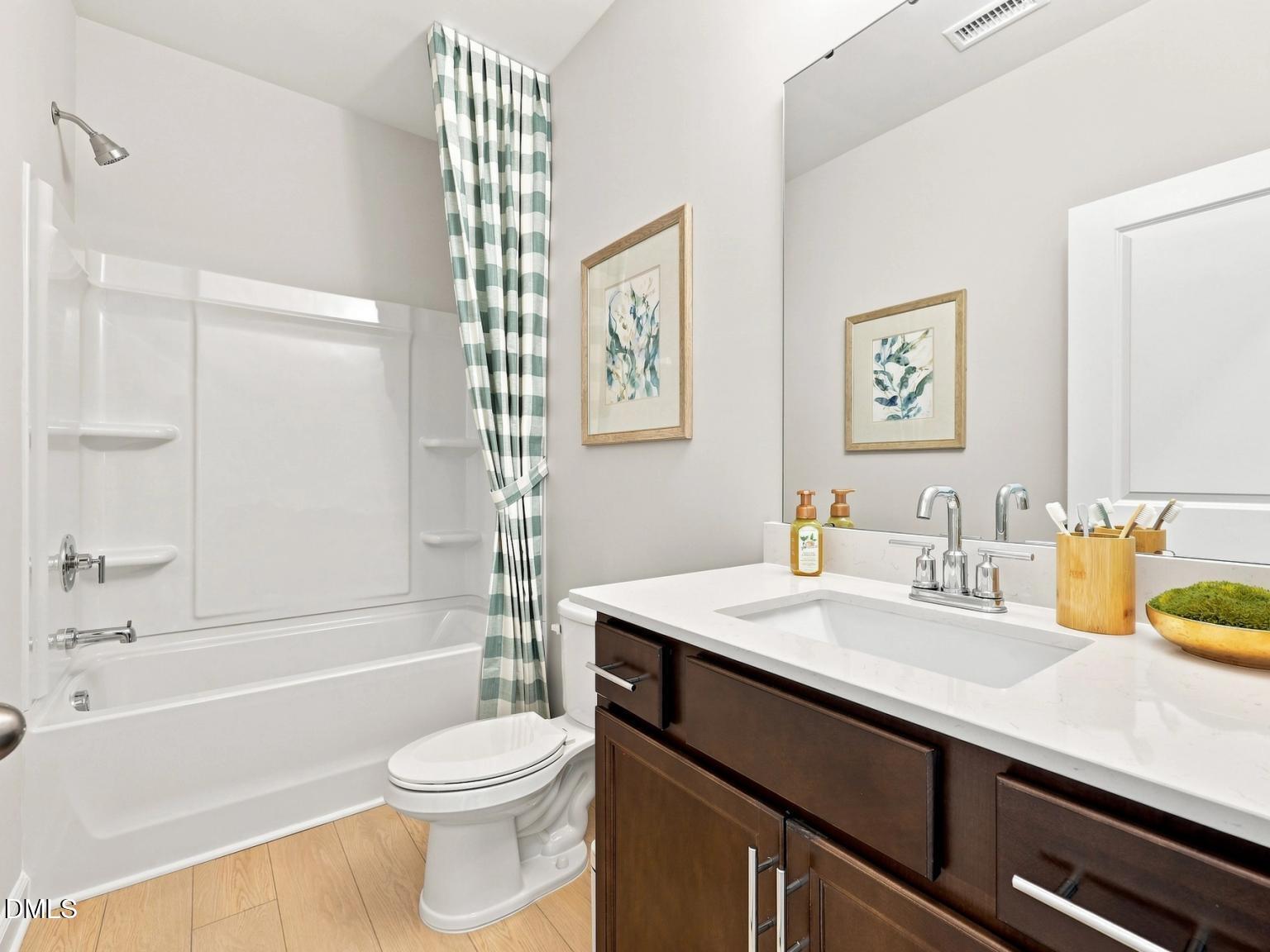 Modern bathroom with white tub-shower combo and dark wood vanity in The Daphne C floor plan at Woodland Crossing, Zebulon.