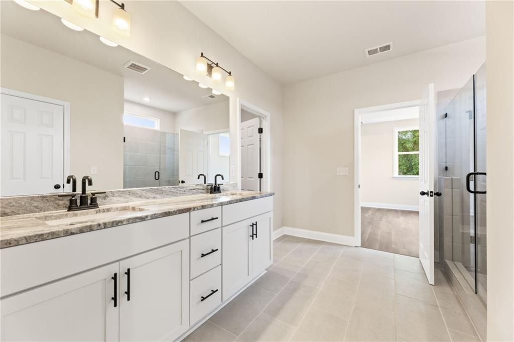 Luxurious master bath with double vanity, quartz counters, white cabinets, and glass shower in Davidson Homes Harrison H, Winder, GA