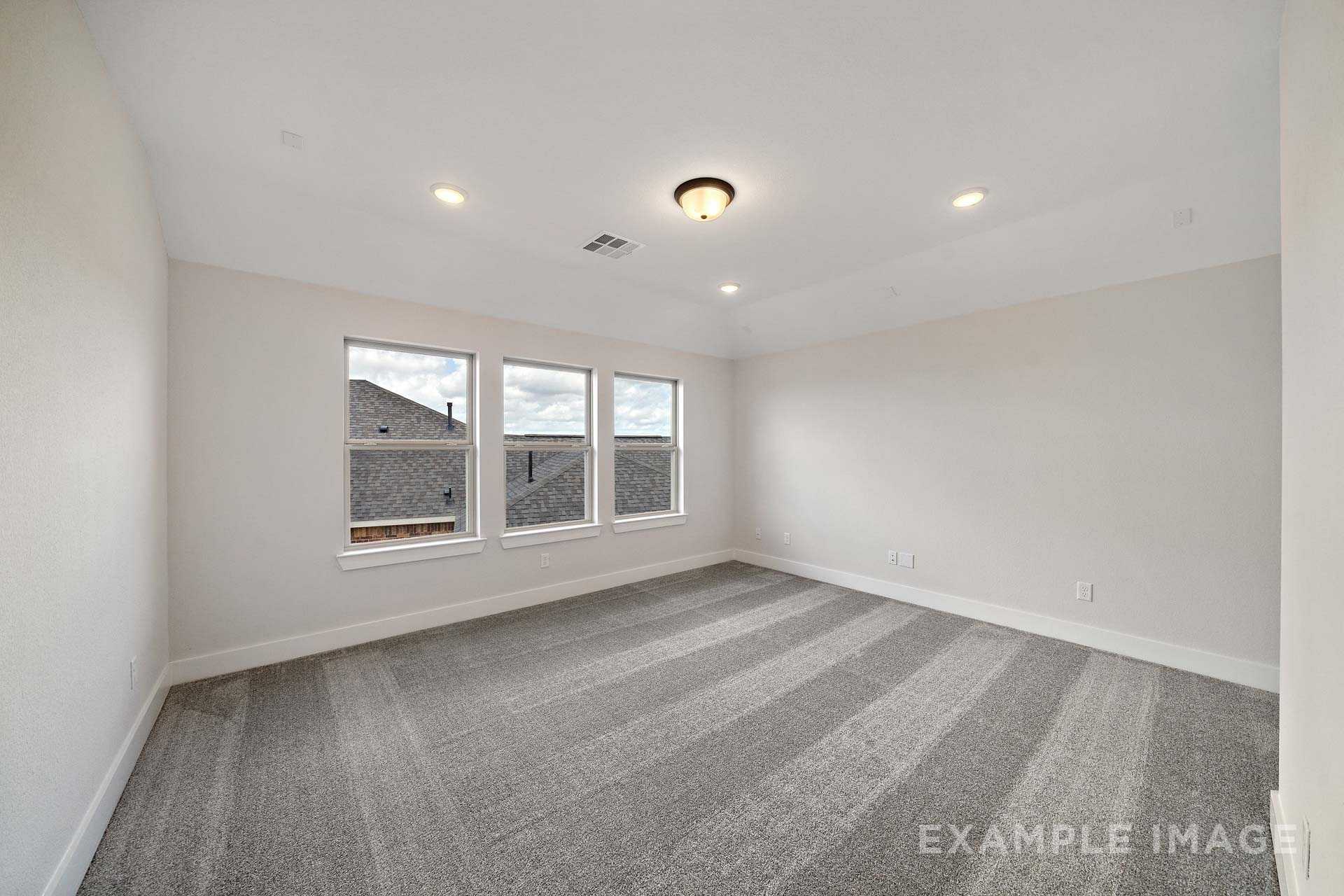 Spacious master bedroom in The Victoria A featuring large triple windows, neutral beige walls, recessed lighting, and plush gray carpet