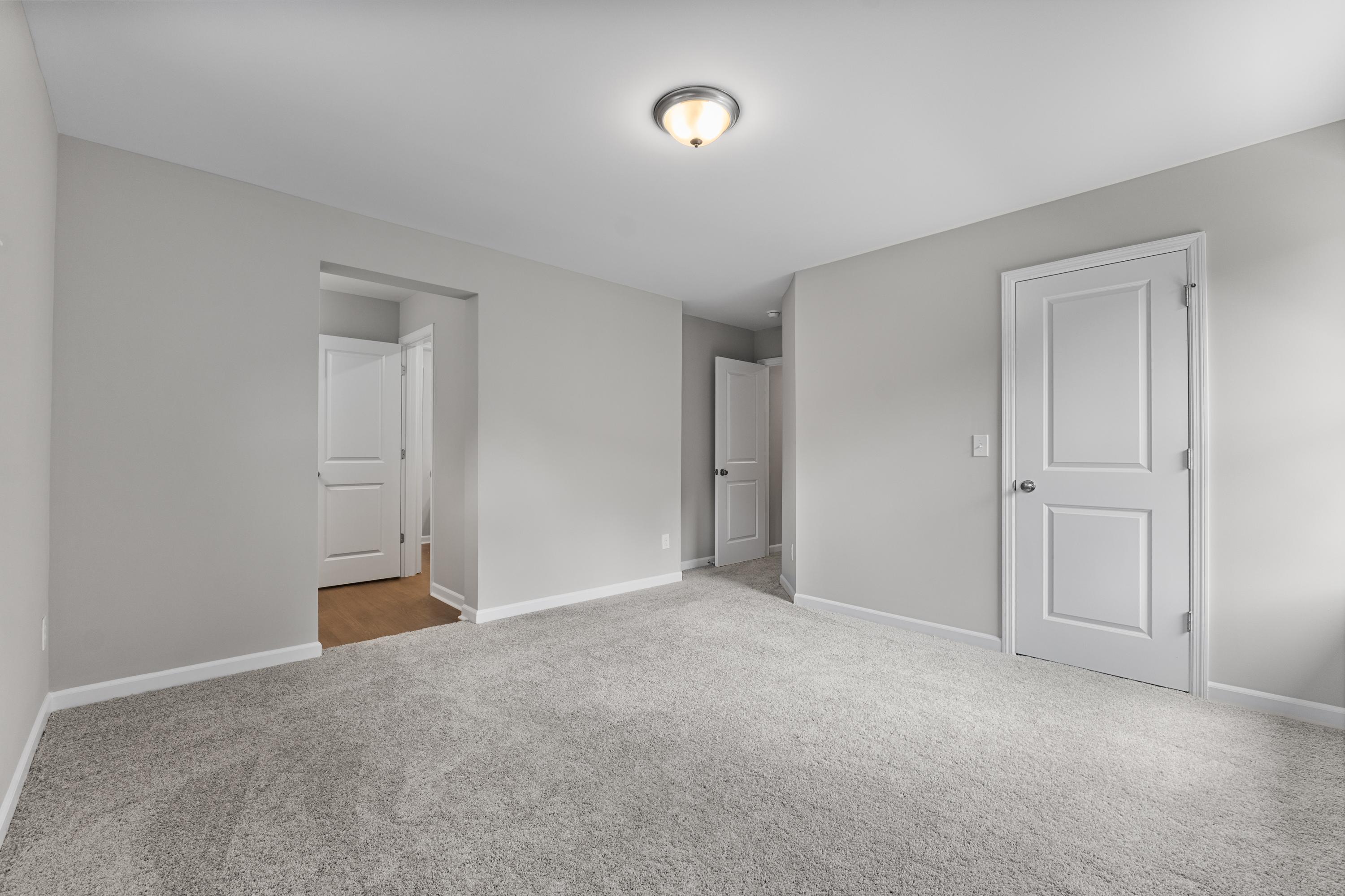 Neutral bedroom interior in The Avalon D with gray walls, plush carpet flooring, white doors, and open archway