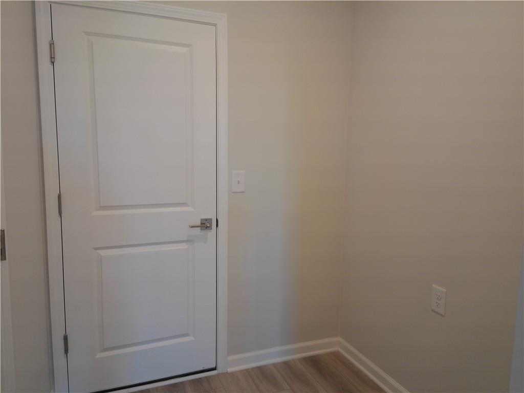 Bright secondary bedroom with white paneled door, beige walls, and light wood floors in Davidson Homes The Marion C, Winder, GA