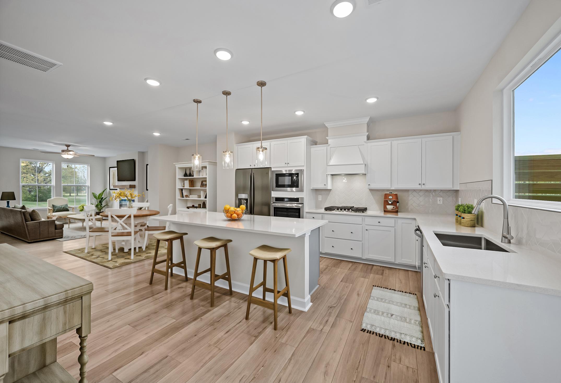 Open-concept gourmet kitchen in The Avery featuring a large quartz island, white cabinetry, and spacious dining area.