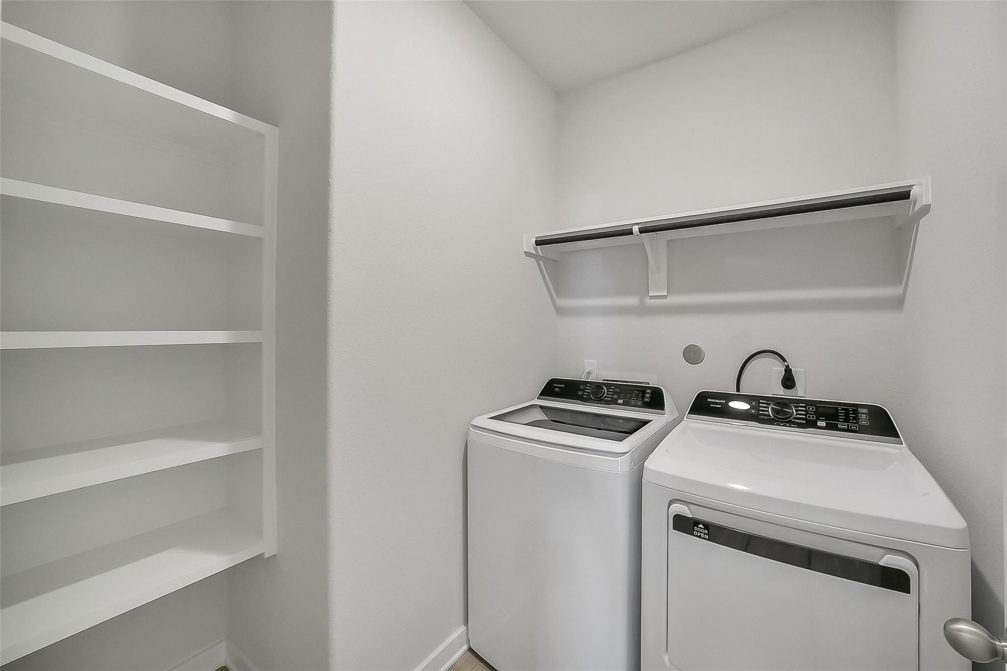 Modern laundry room with white washer, dryer, built-in shelving, and utility sink in Davidson Homes The Acadia A, Katy, Texas