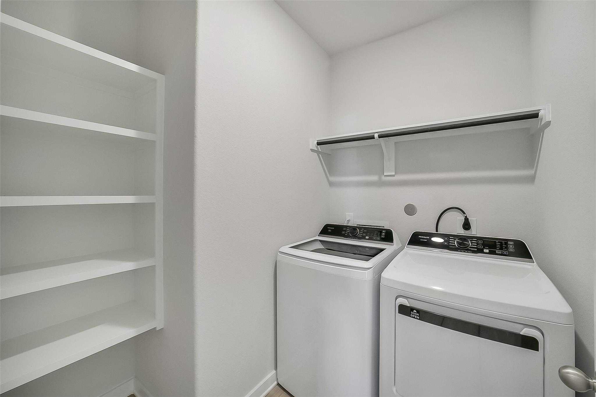 Modern laundry room with white washer, dryer, built-in shelving, and utility sink in Davidson Homes The Acadia A, Katy, Texas