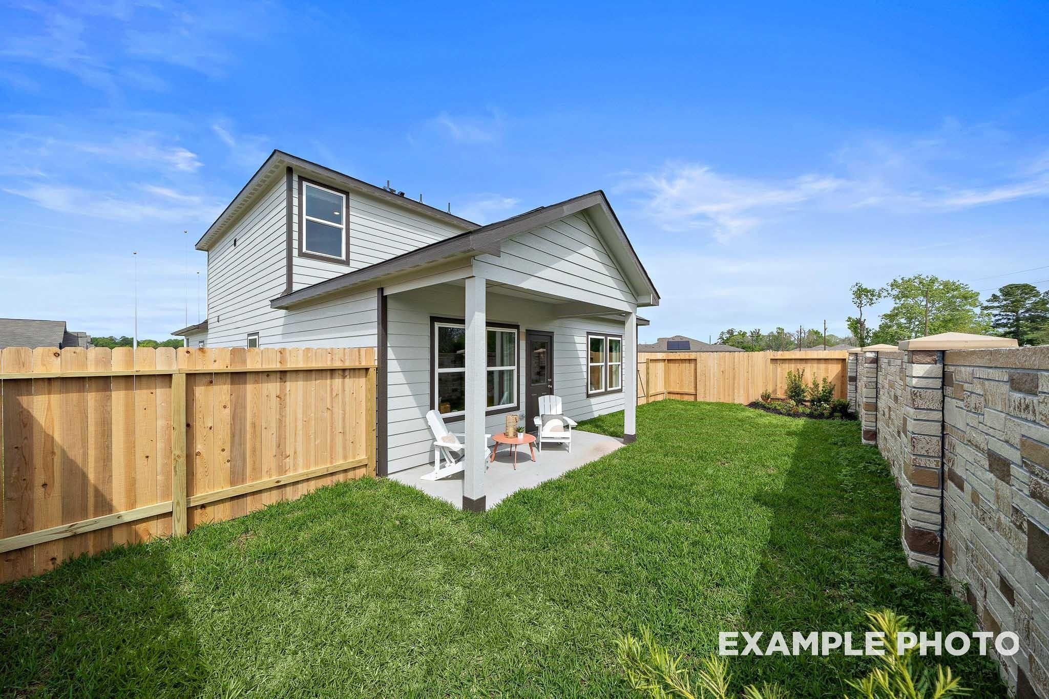 Two-story Sabine F home exterior with covered porch, white chairs, and lush fenced backyard in Windmill Estates, Magnolia, Texas