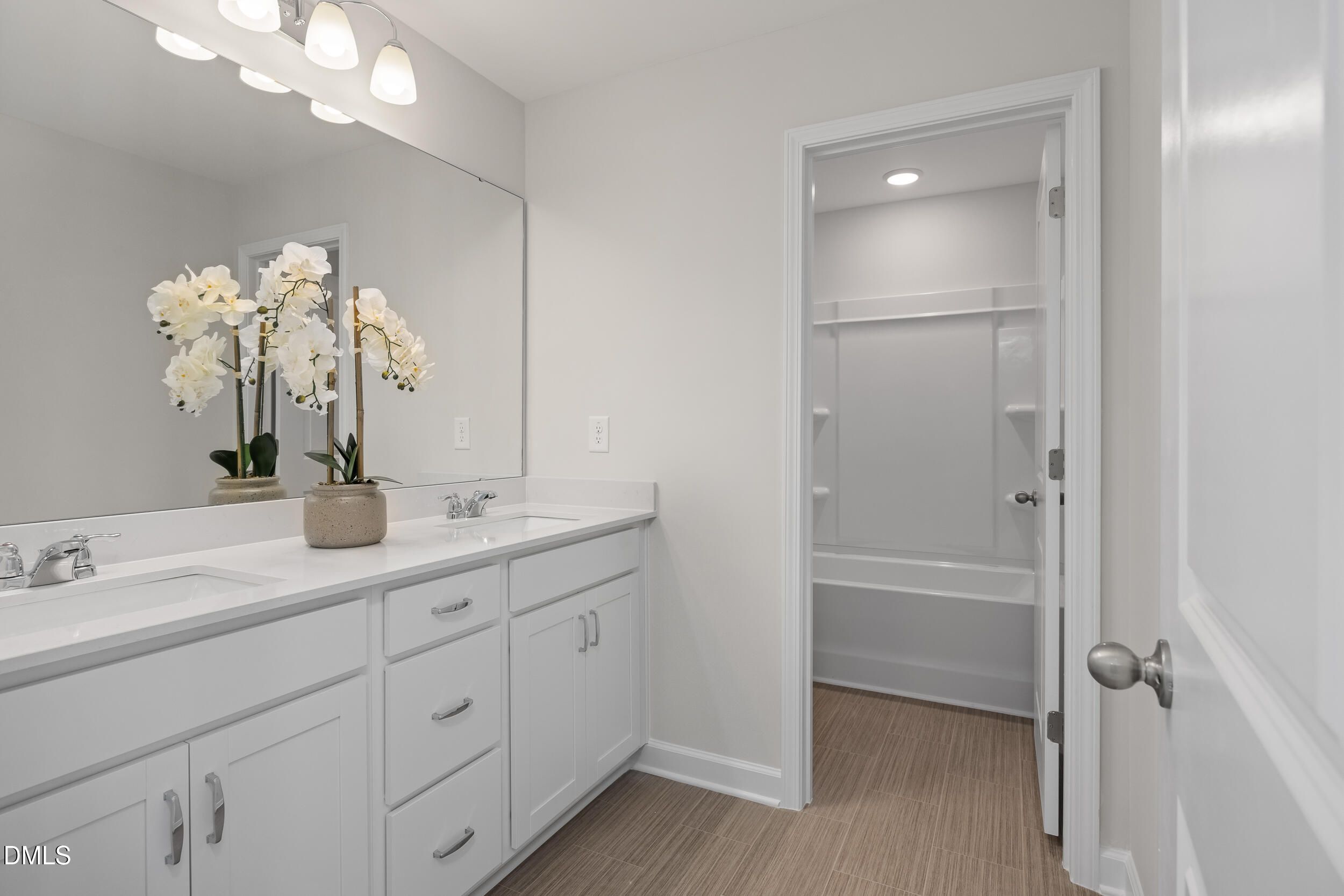 Elegant master bathroom with double white vanity, orchids, large mirror, and tub-shower in Davidson Homes The Preston C, Lillington, NC