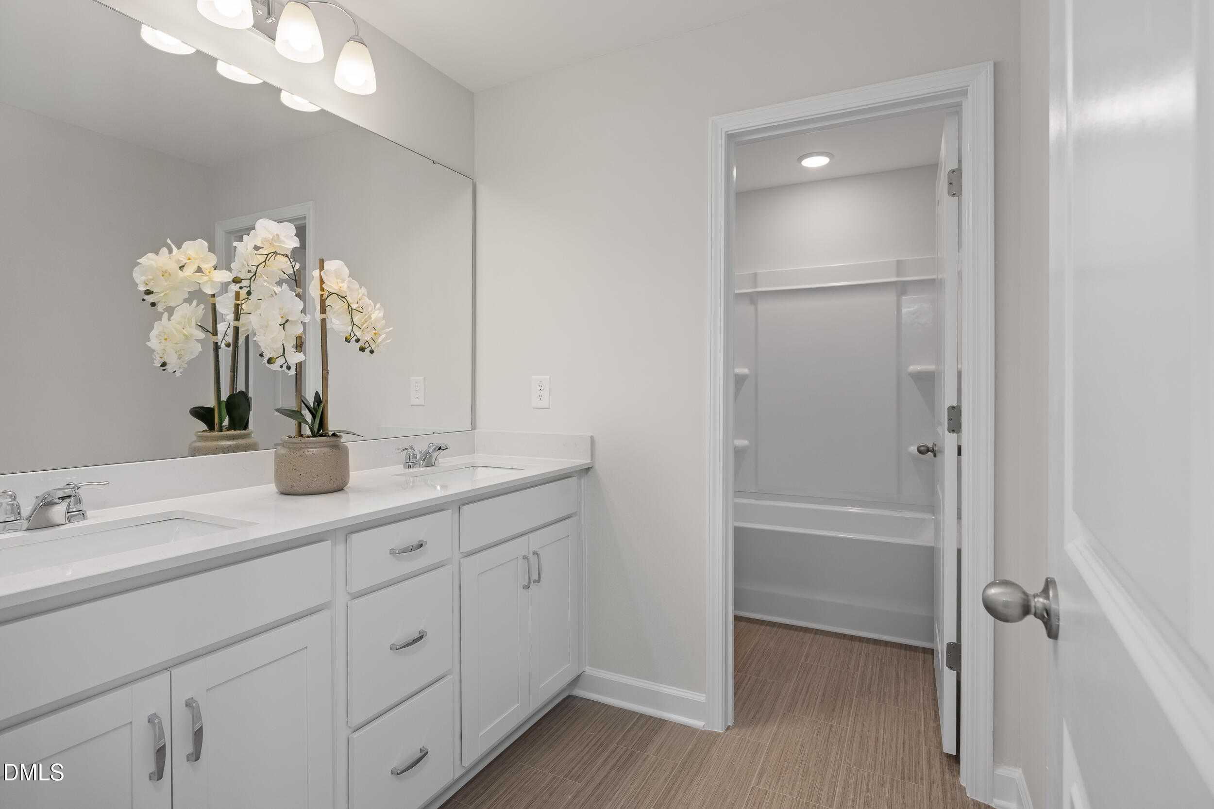 Elegant master bathroom with double white vanity, orchids, large mirror, and tub-shower in Davidson Homes The Preston C, Lillington, NC