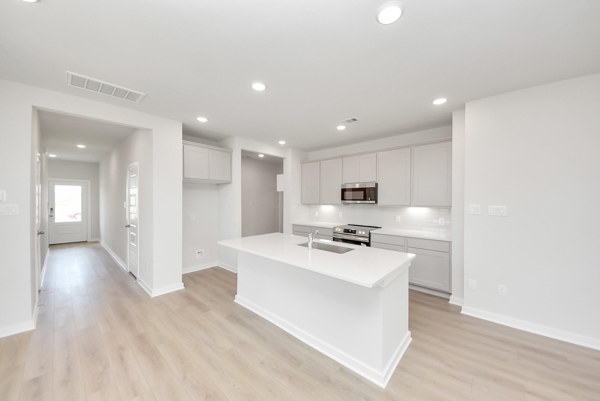 Modern kitchen with white island, light cabinetry, and stainless appliances in The Blanco F home at Spring Branch Crossing.