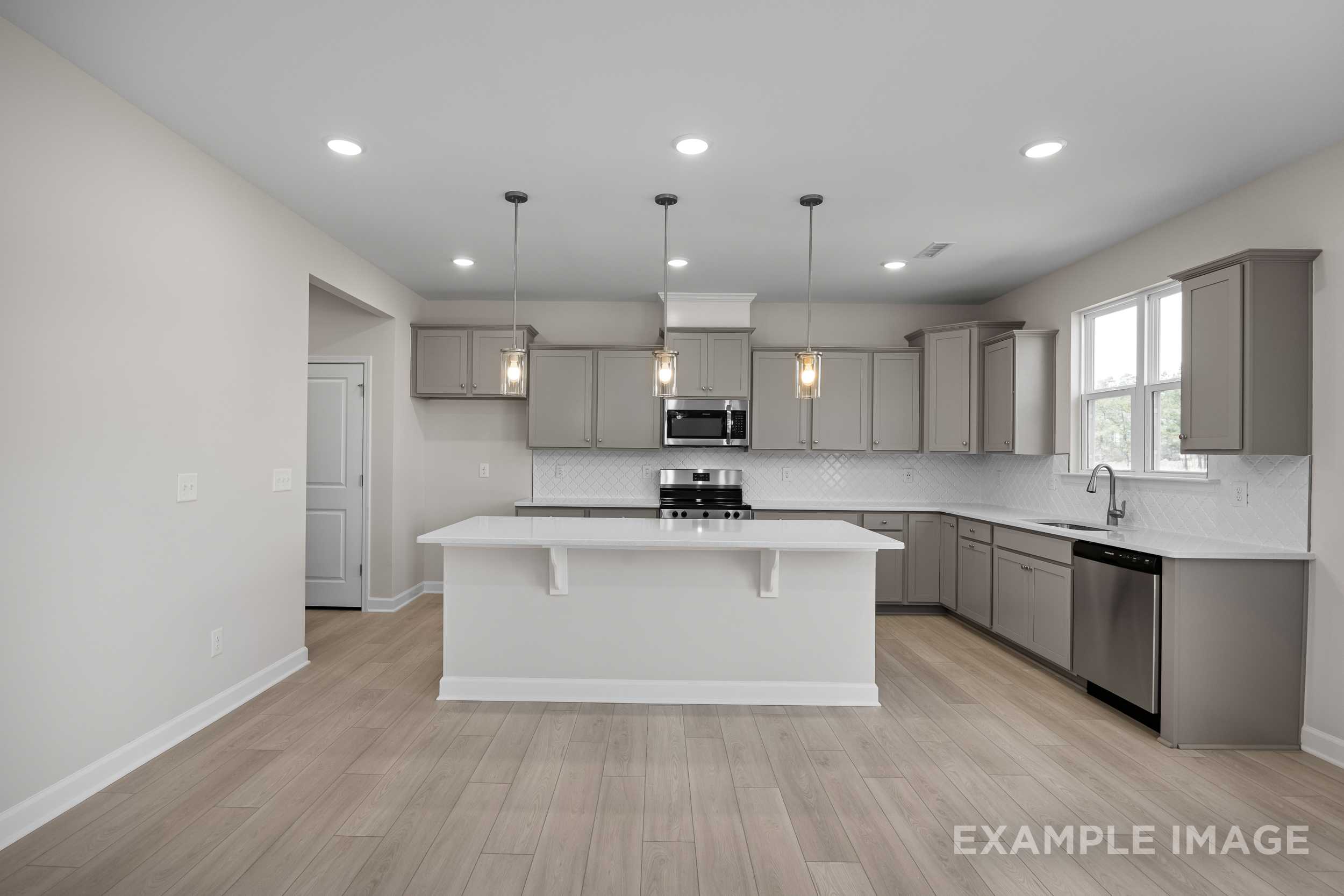 Spacious Hickory II kitchen with large white island, gray shaker cabinets, stainless appliances, and open wood-floor layout