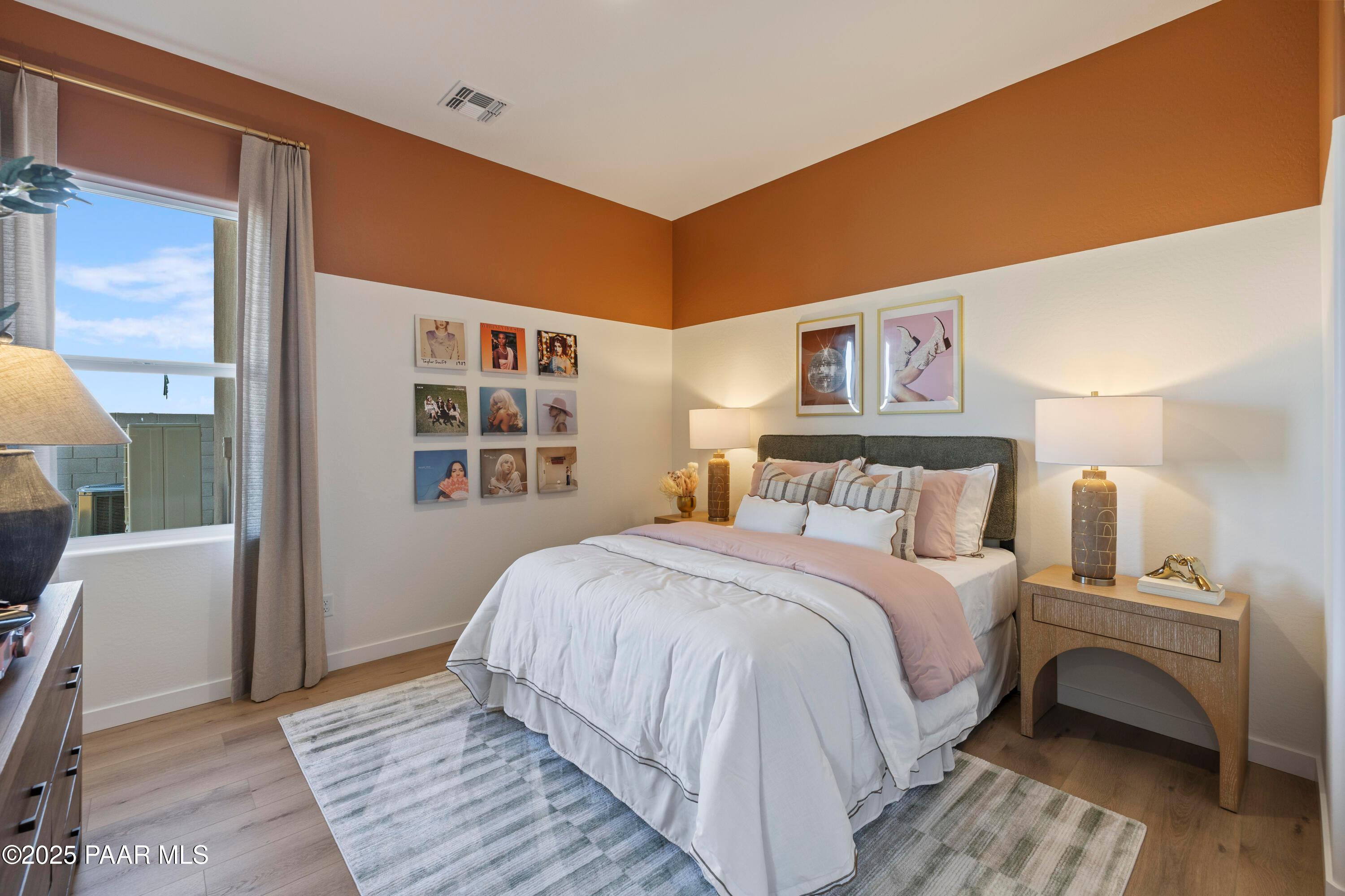 Cozy bedroom with white tufted bed, pink pillows, orange accent wall, and large windows in Davidson Homes The Blaze D, Prescott AZ