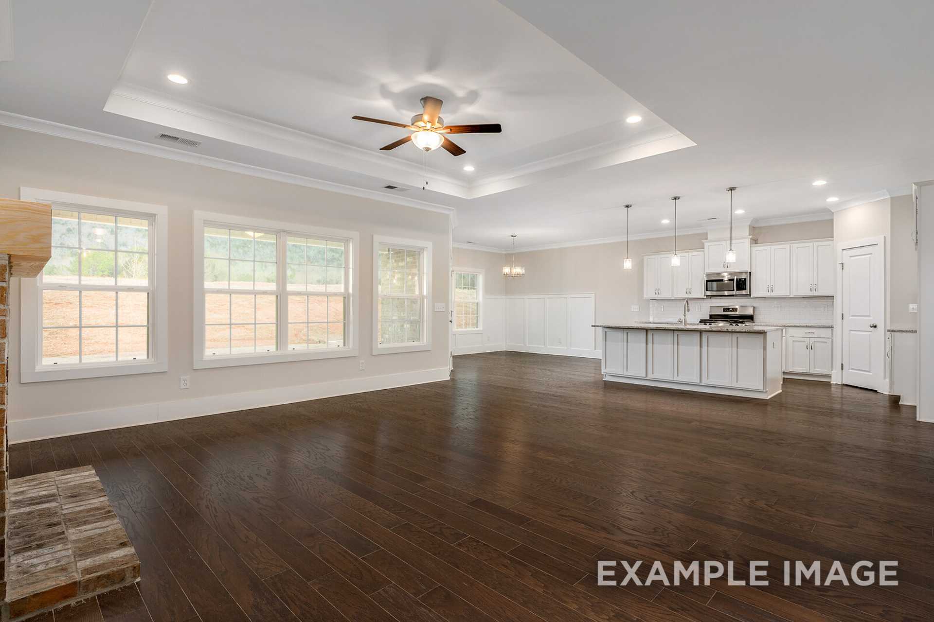 Spacious open-concept kitchen and living area in The Rockford home featuring hardwood floors, brick fireplace, white cabinetry, and large windows