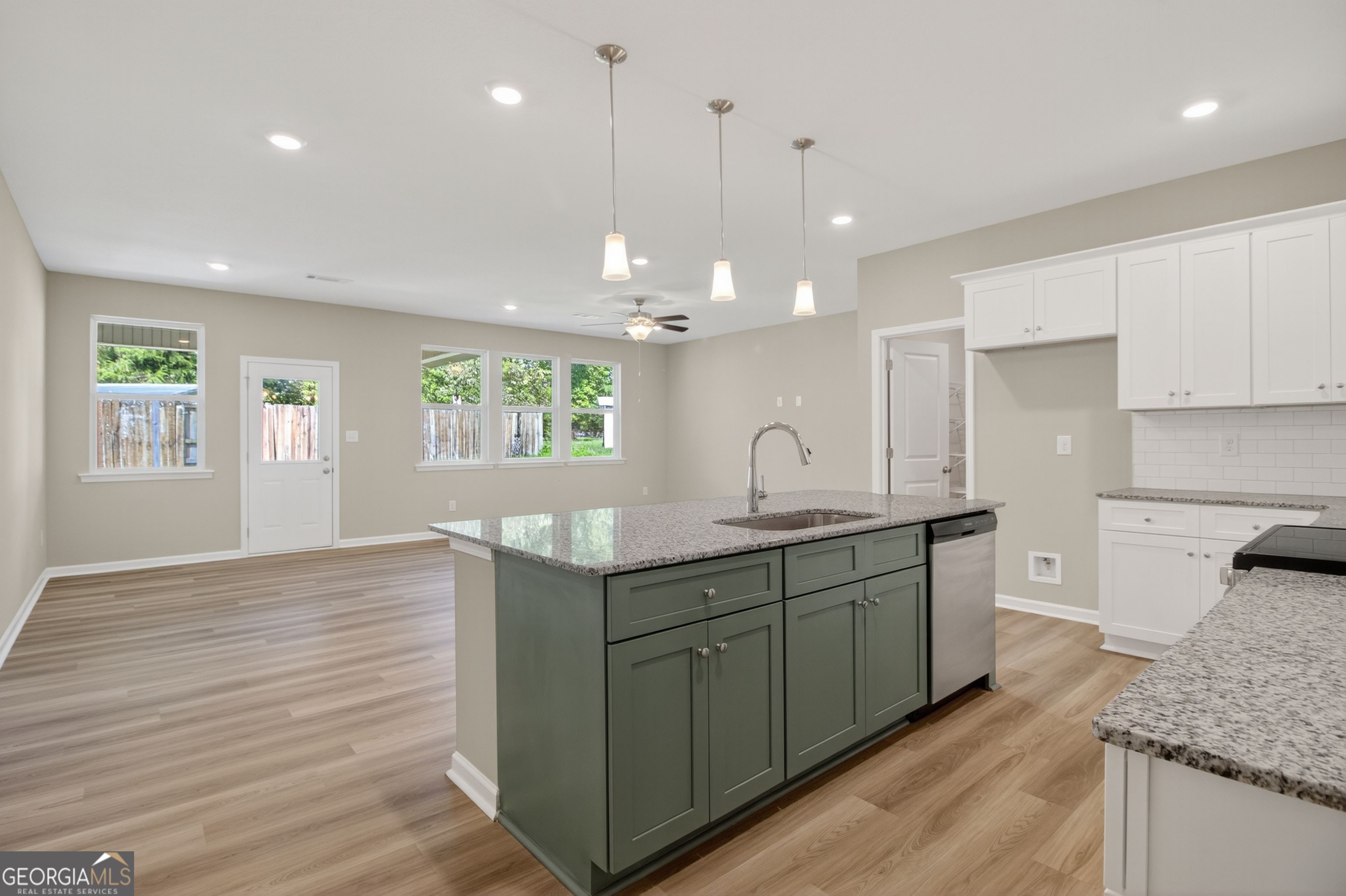 Modern open kitchen with white shaker cabinets, green island, granite counters, stainless sink in Evermore Homes The Luna, Perry, Georgia