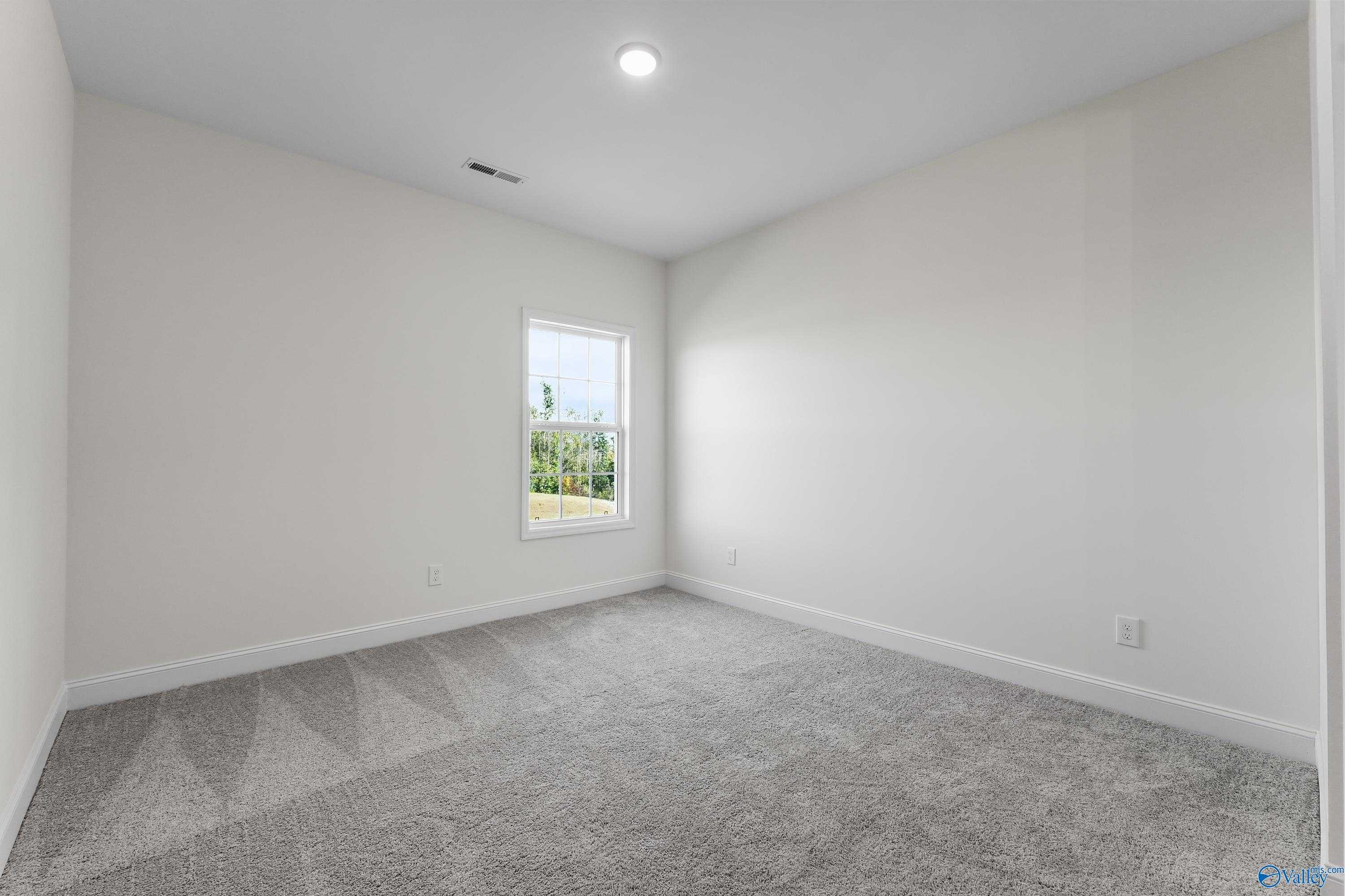 Empty bedroom with beige walls, gray carpet, and window overlooking trees in Davidson Homes The Finleigh, Harvest, Alabama