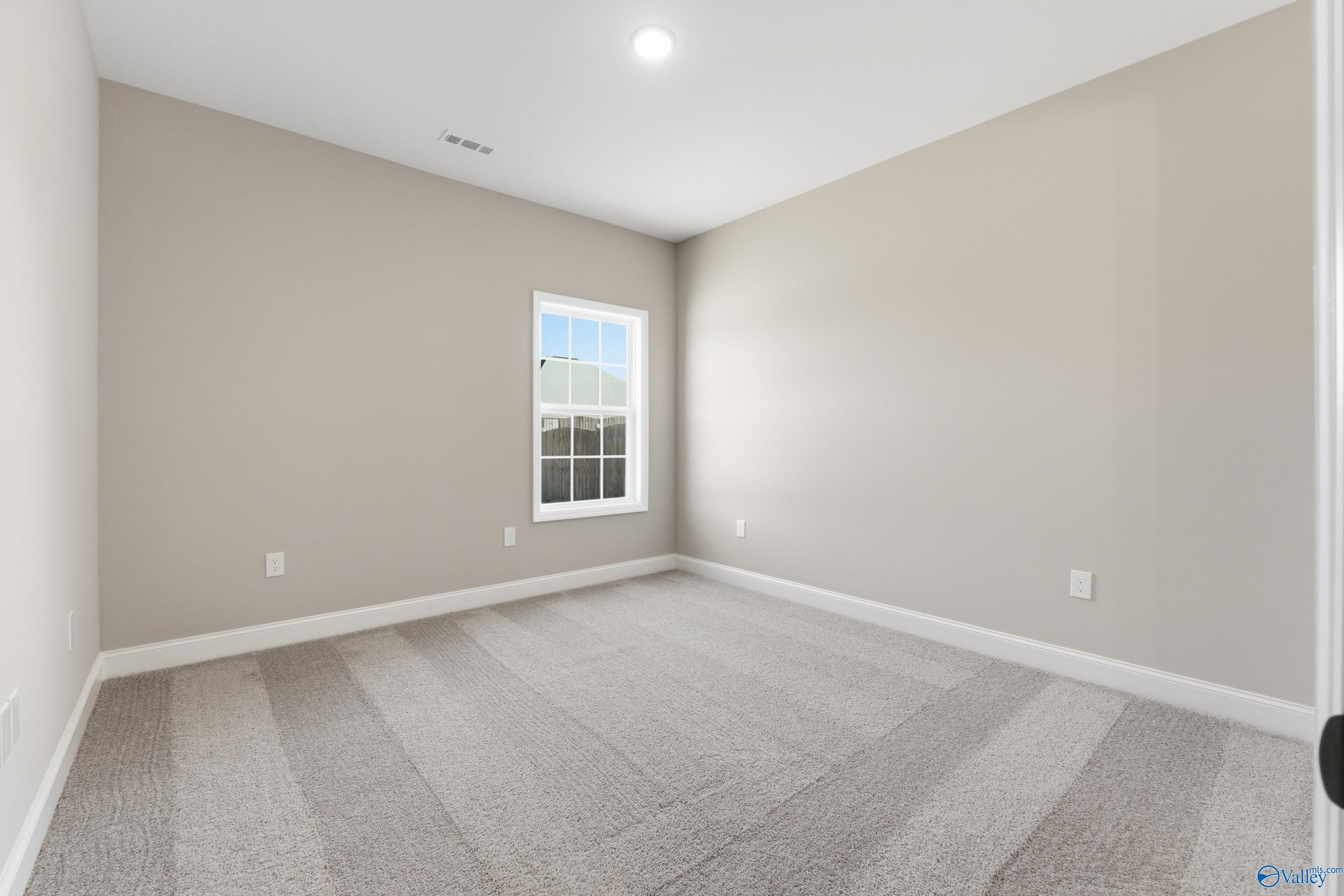 Bright secondary bedroom with beige walls, large window, and carpeted floor in The Finleigh 3-bedroom home, Meridianville, Alabama