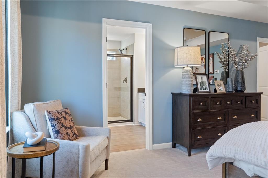 Cozy master bedroom with light blue walls, tufted armchair, dark wood dresser, and en-suite shower in Davidson Homes The Marion B, Kennesaw, GA