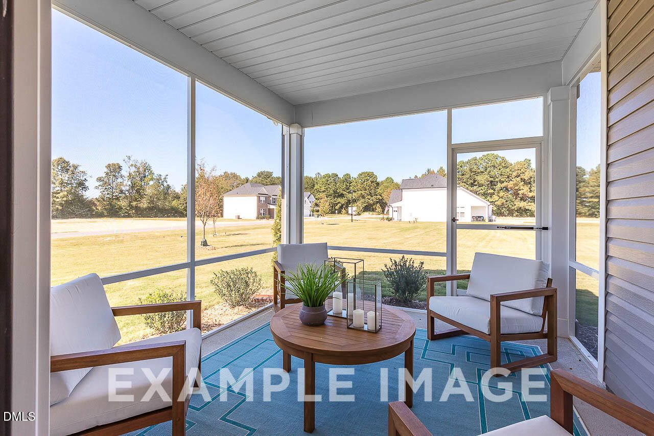 Screened-in back porch with white cushioned seating and wooden table overlooking backyard in Davidson Homes The Ash C, Lillington NC