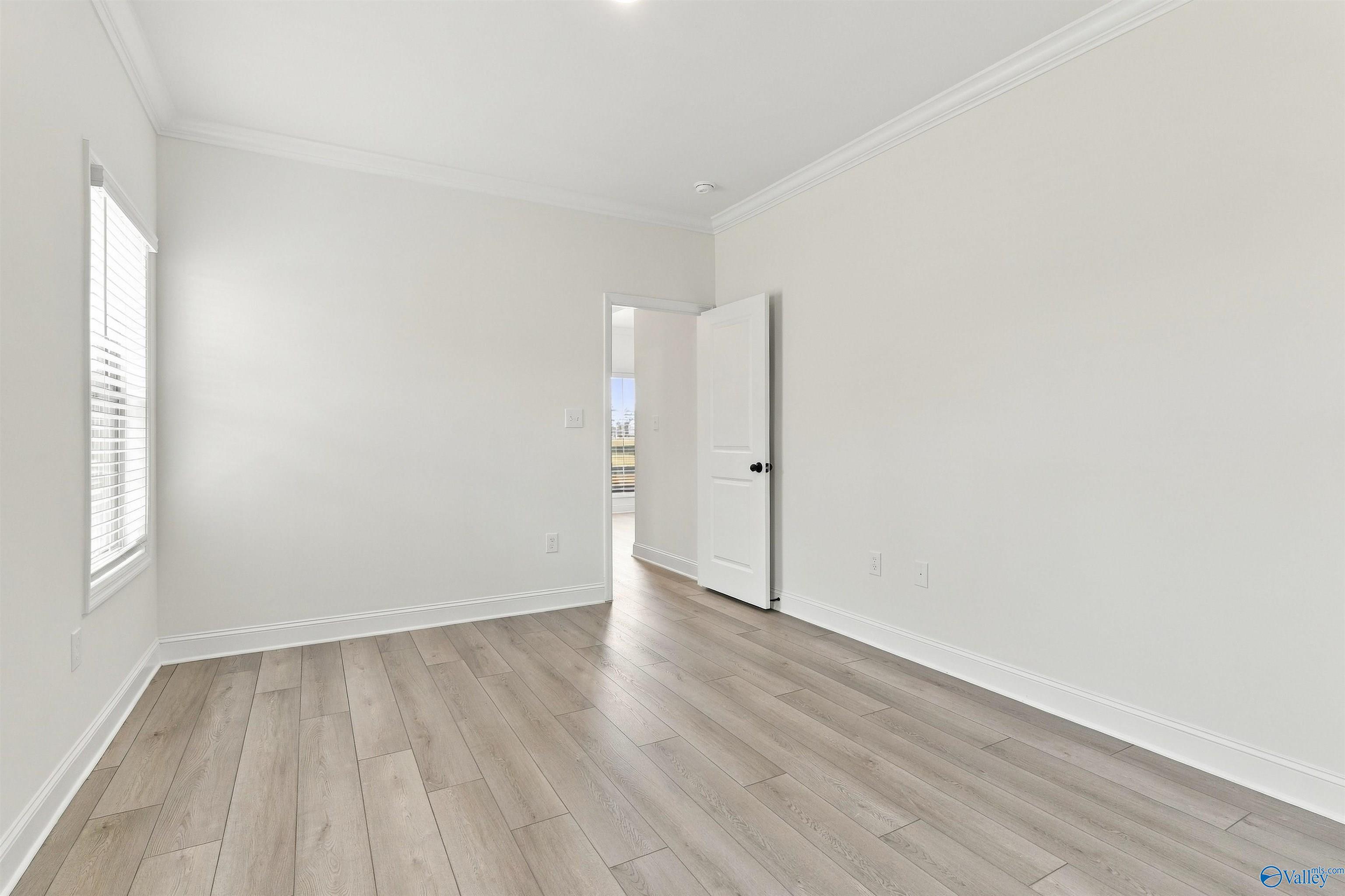 Bright empty bedroom with wood-look flooring and white crown molding in The Valencia with Bonus at Riverton Preserve, Huntsville, Alabama