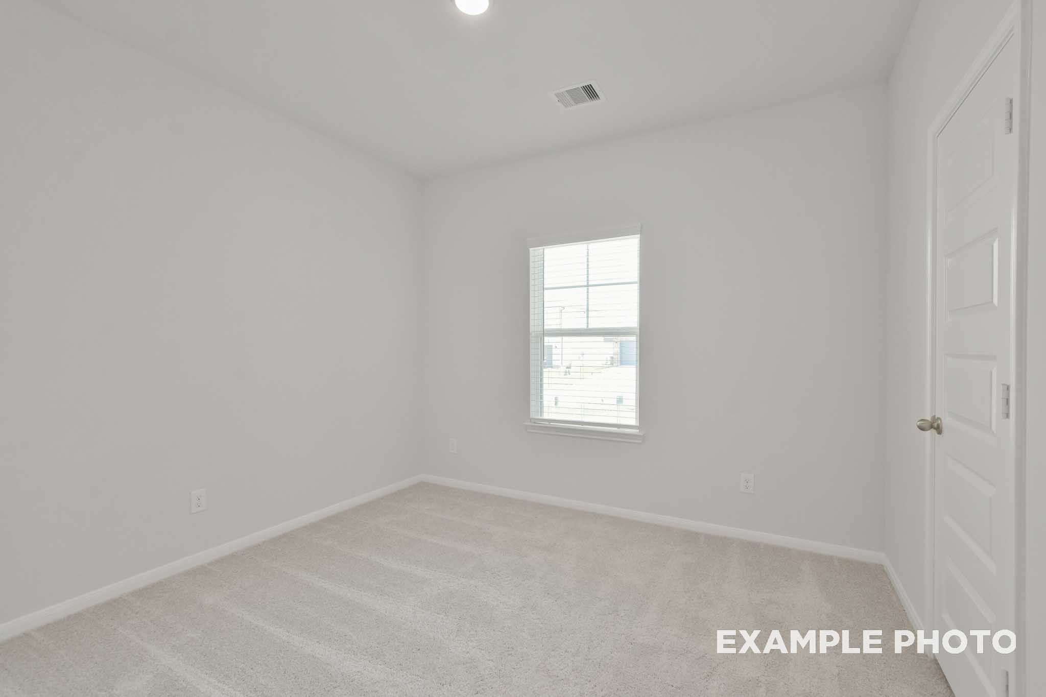 Spacious secondary bedroom in The Comal G home design with white walls, beige carpet, large window, and neutral finishes