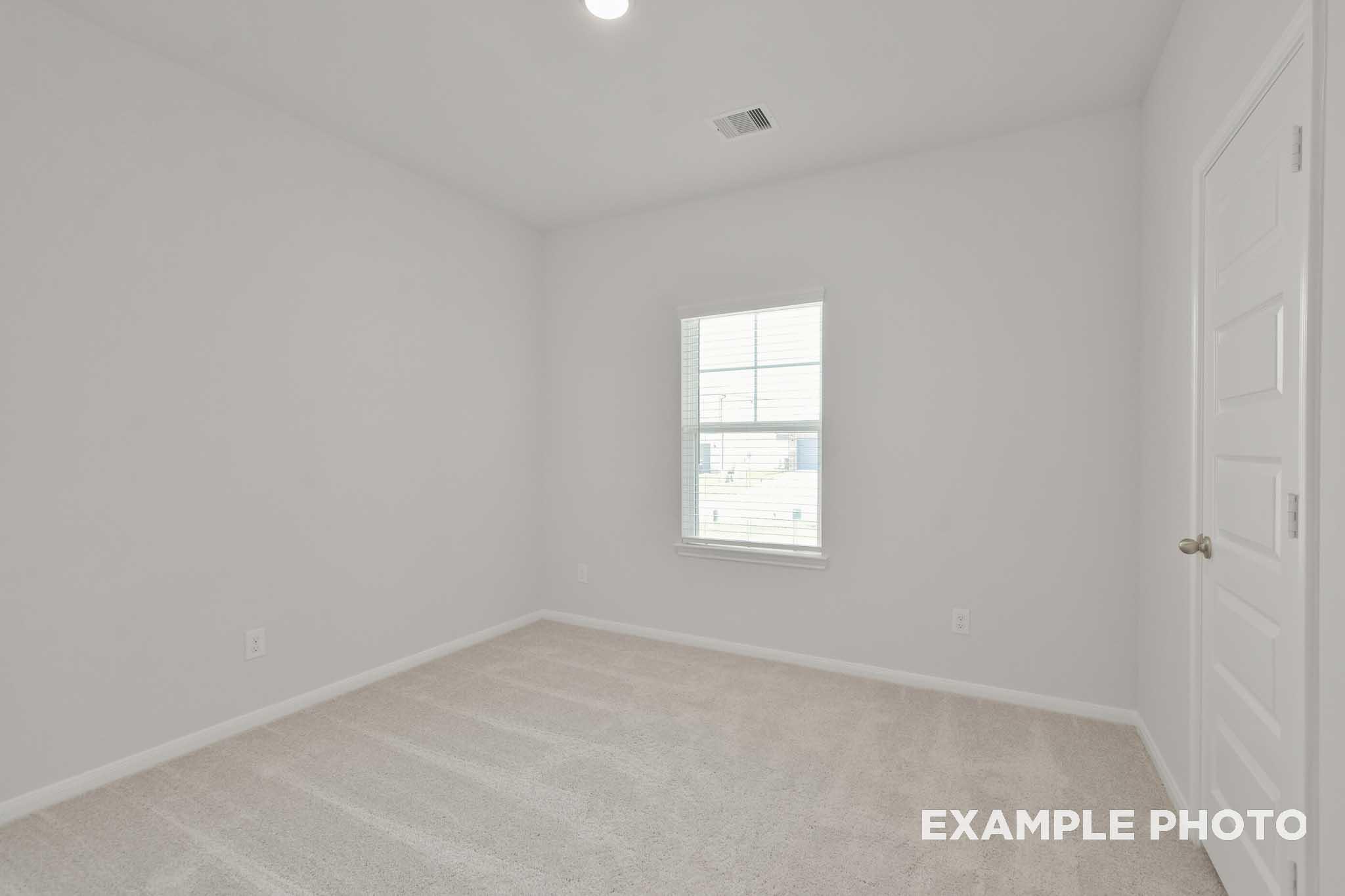 Spacious secondary bedroom in The Comal G home design with white walls, beige carpet, large window, and neutral finishes