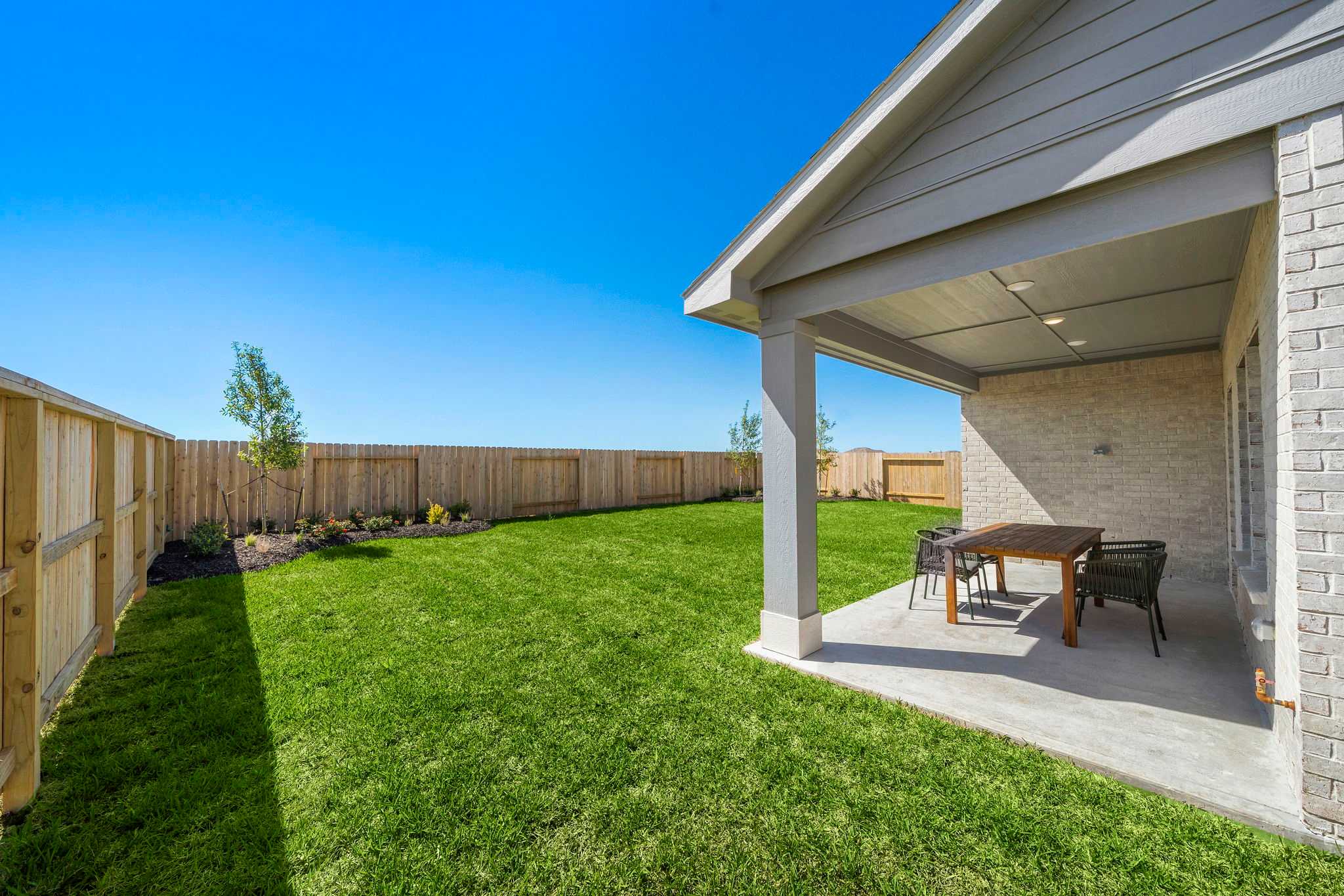 Covered patio with outdoor dining at River Ranch Meadows in Dayton Texas, lush green lawn and wooden fence