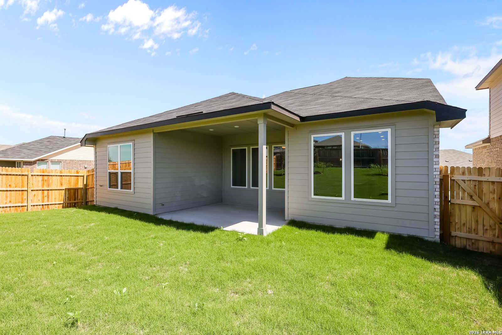 Covered back patio with large windows on gray-sided Sequoia B home, fenced green yard in Comanche Ridge, San Antonio, Texas