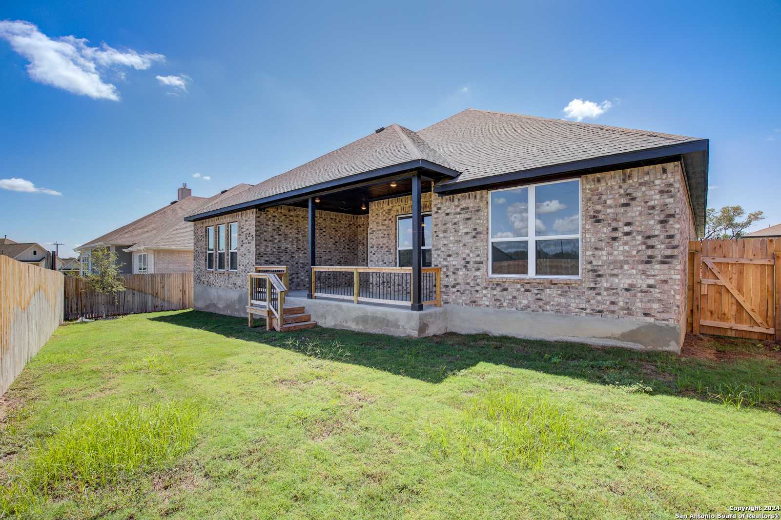 Rear view of brick 4-bedroom home with covered patio, large windows, and lush green backyard in The Reserve at Potranco Oaks, Castroville, Texas
