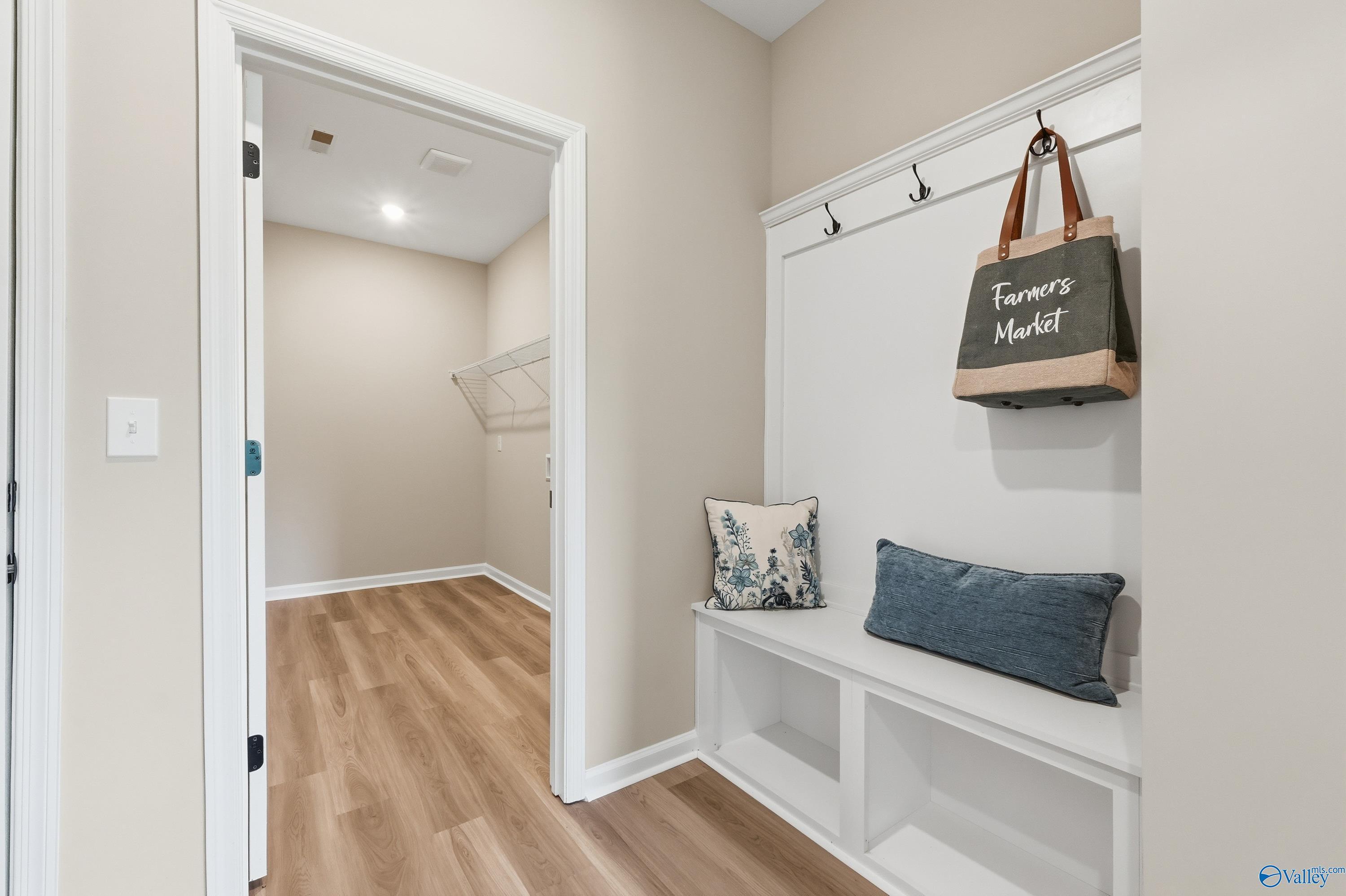 Cozy mudroom with white built-in bench, storage cubbies, wall hooks, tote bag, and pillows in Davidson Homes The Dorado, Riverton Preserve, Huntsville AL