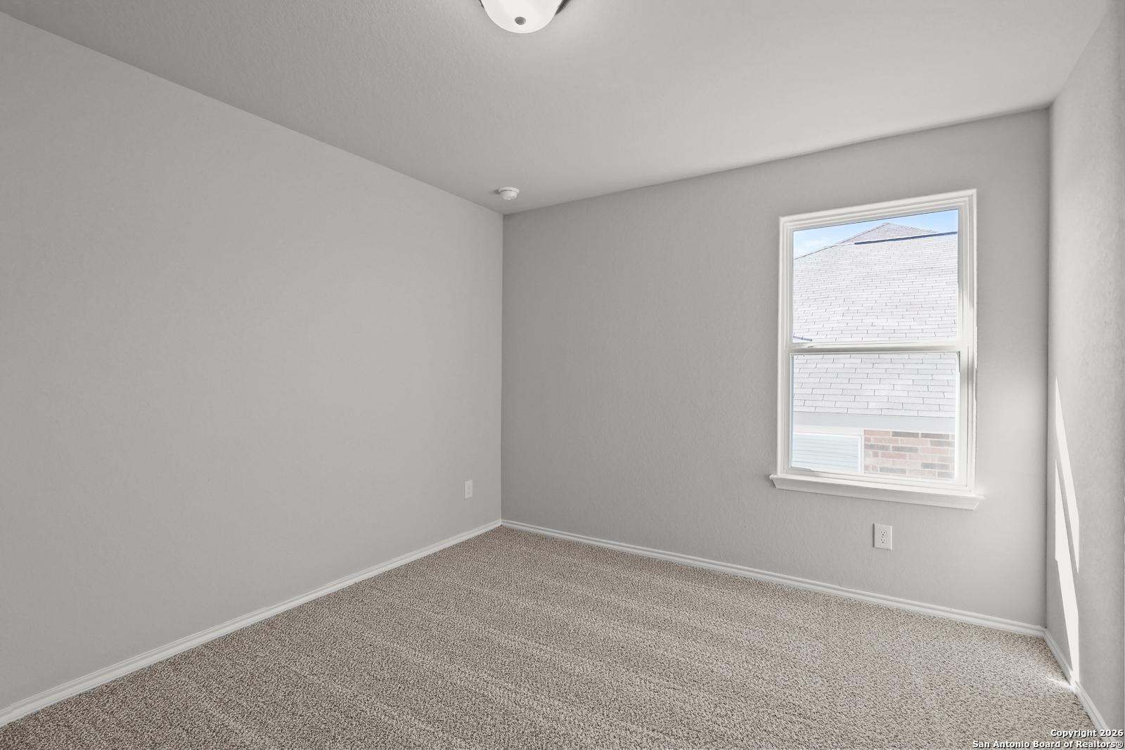 Bright secondary bedroom with gray walls, beige carpet, large window, and neutral tones in Davidson Homes The Murray K, San Antonio