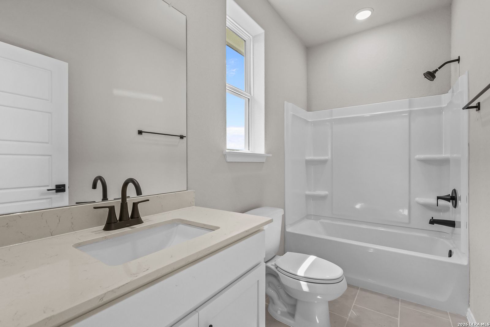 Modern bathroom with white vanity, quartz countertop, and tub-shower combo in The Daphne H home at Hannah Heights, Seguin.