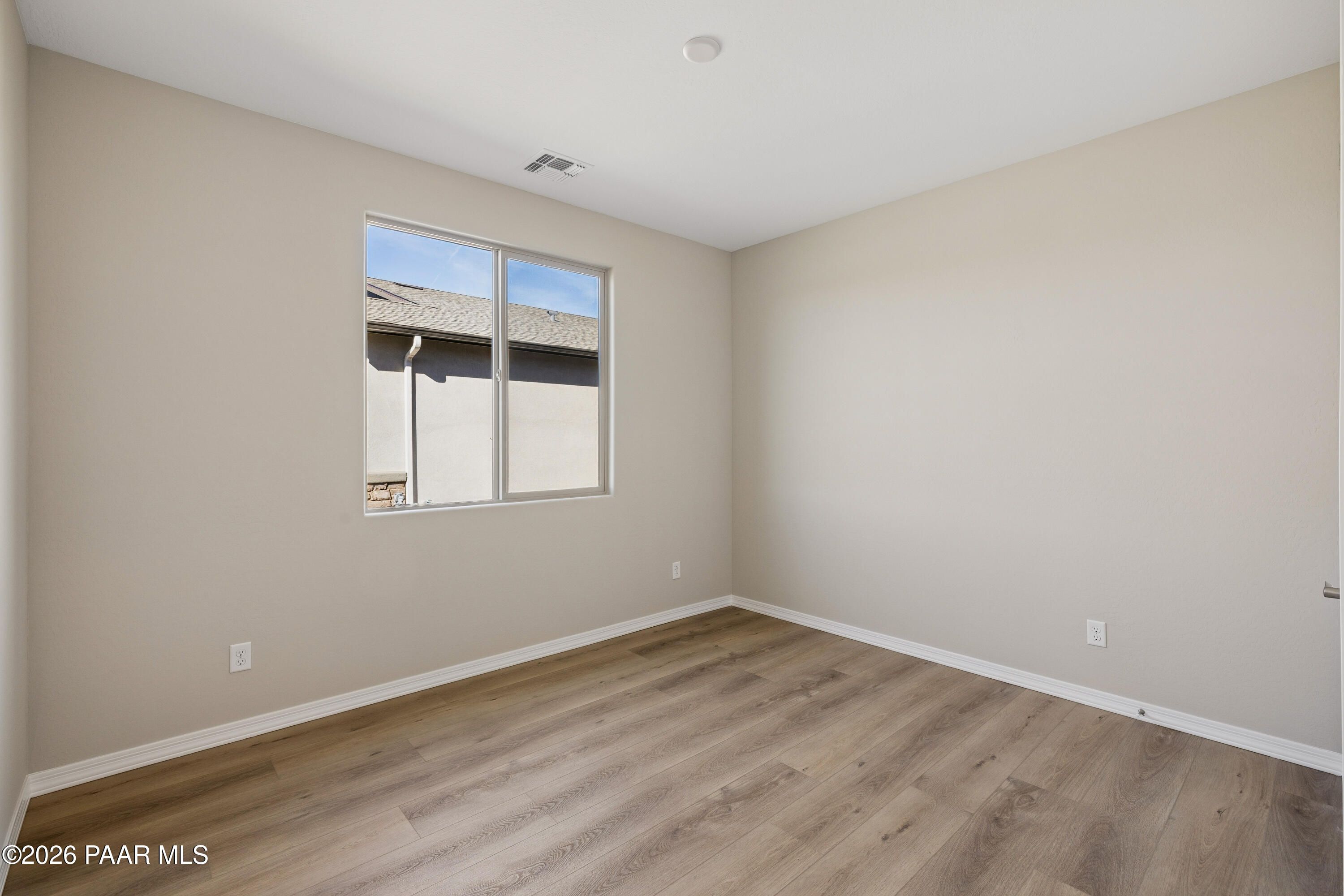 Bright bedroom with beige walls, large sunny window, and luxury vinyl plank flooring in Davidson Homes The Harmony A, Prescott Valley, AZ