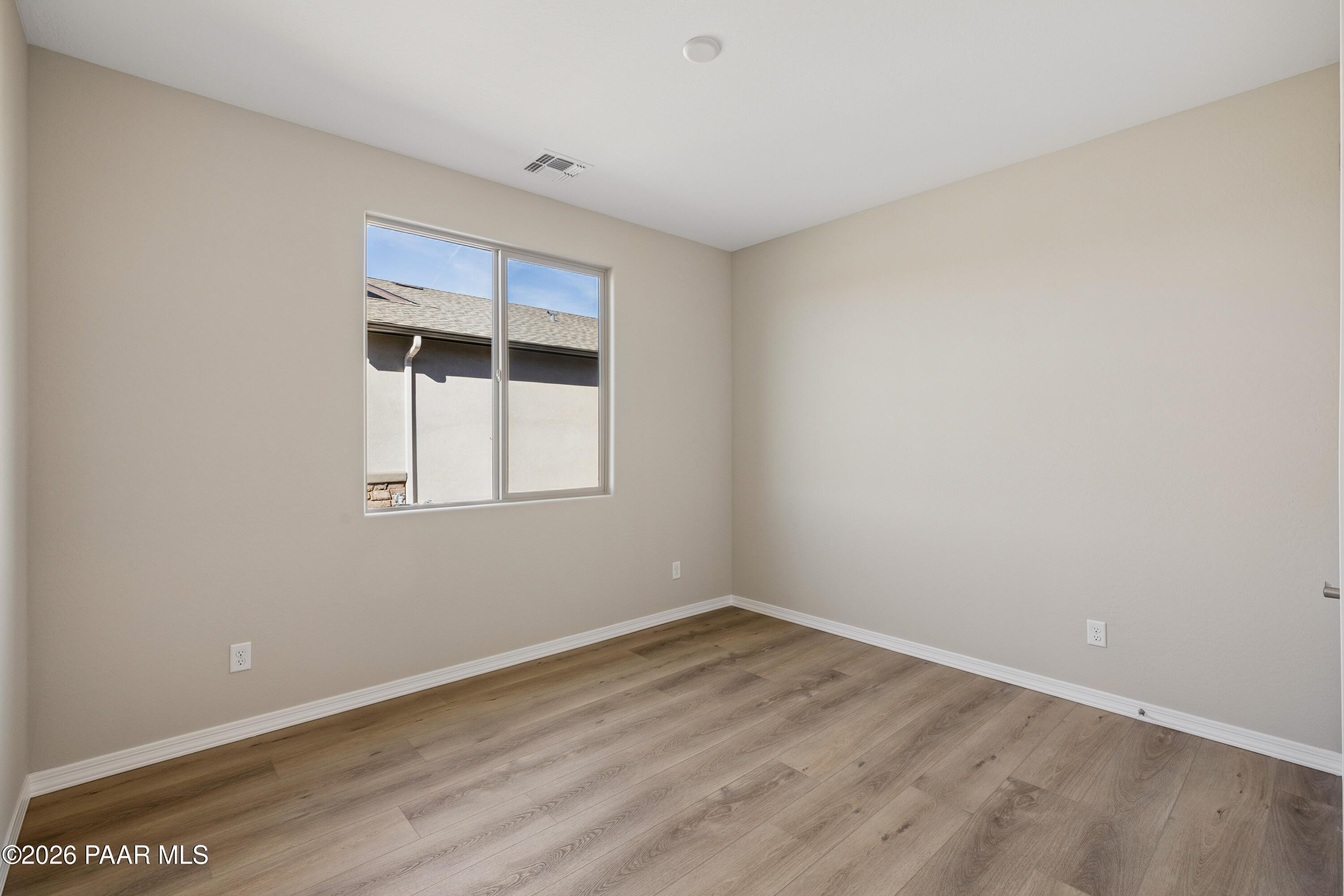 Bright bedroom with beige walls, large sunny window, and luxury vinyl plank flooring in Davidson Homes The Harmony A, Prescott Valley, AZ