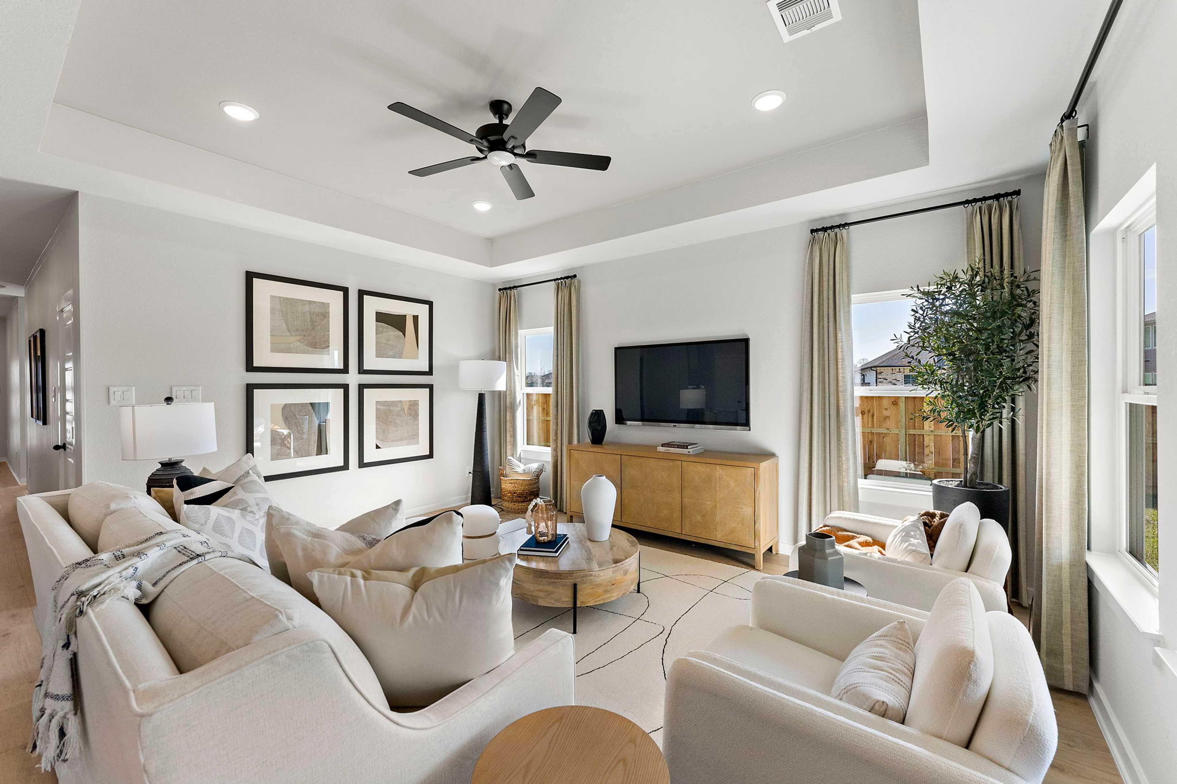 Spacious living room at Sundance Cove in Crosby Texas with beige sectional sofa, wooden TV console, ceiling fan, and large curtained windows