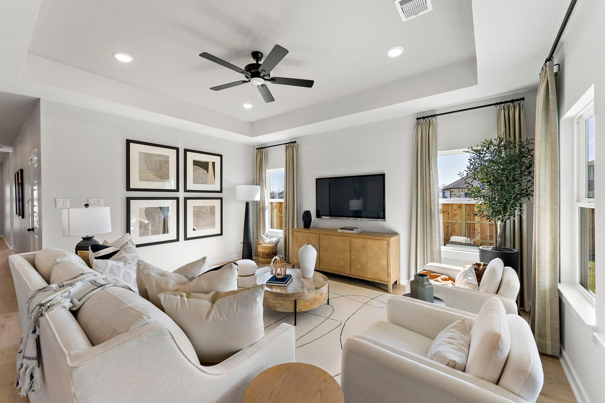 Spacious open-concept living room in Sundance Cove Crosby Texas with neutral gray walls beige sofas ceiling fan TV console and large windows