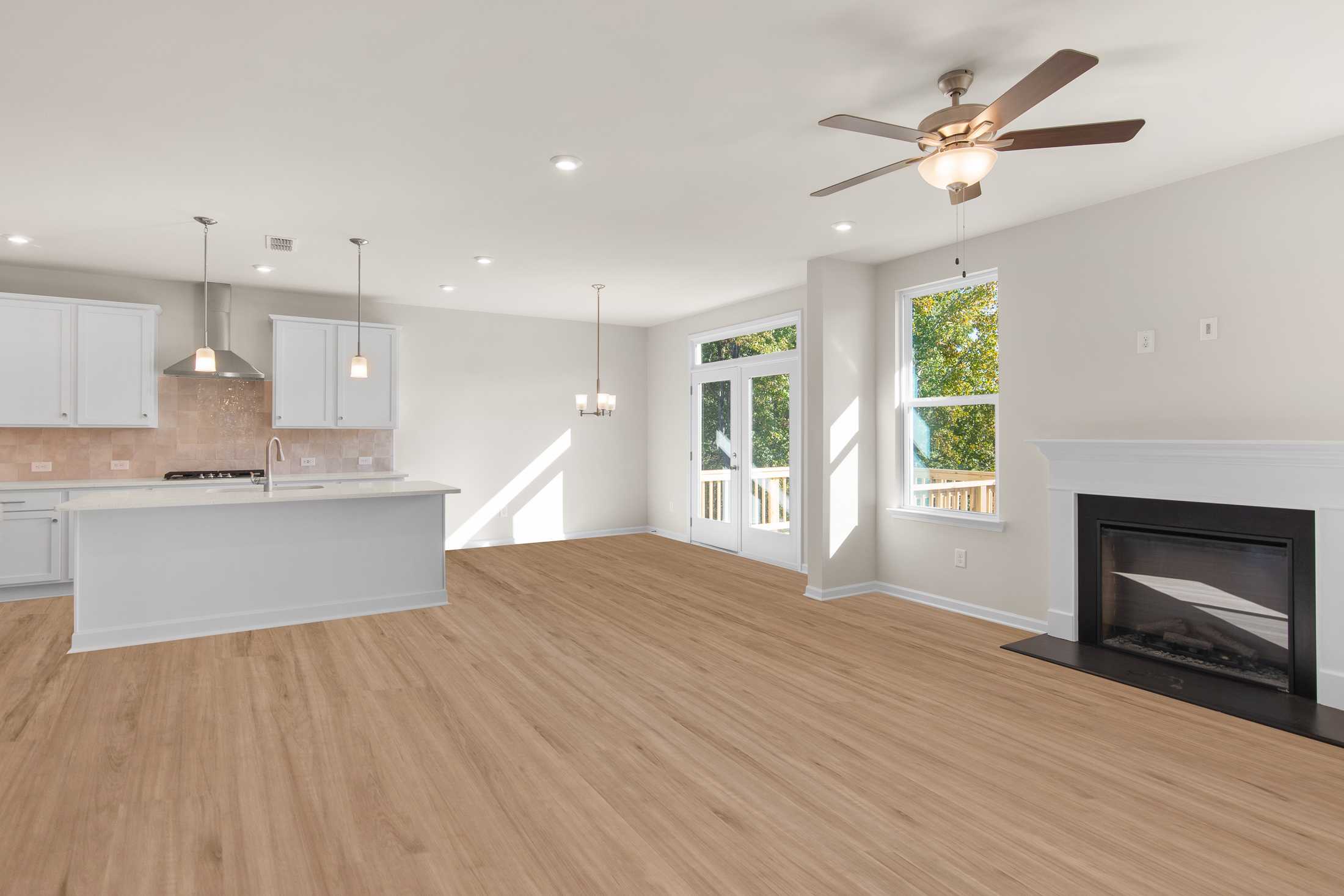 Spacious open-concept kitchen and living area in The Willow B with white island, fireplace, French doors to deck