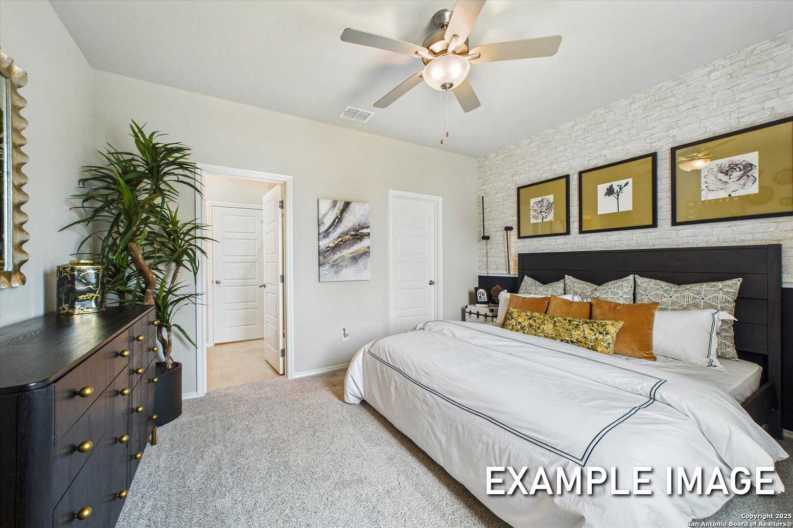 Cozy bedroom with white shiplap wall, ceiling fan, plush white bed, and modern black dresser in Davidson Homes The Sabine C, San Antonio