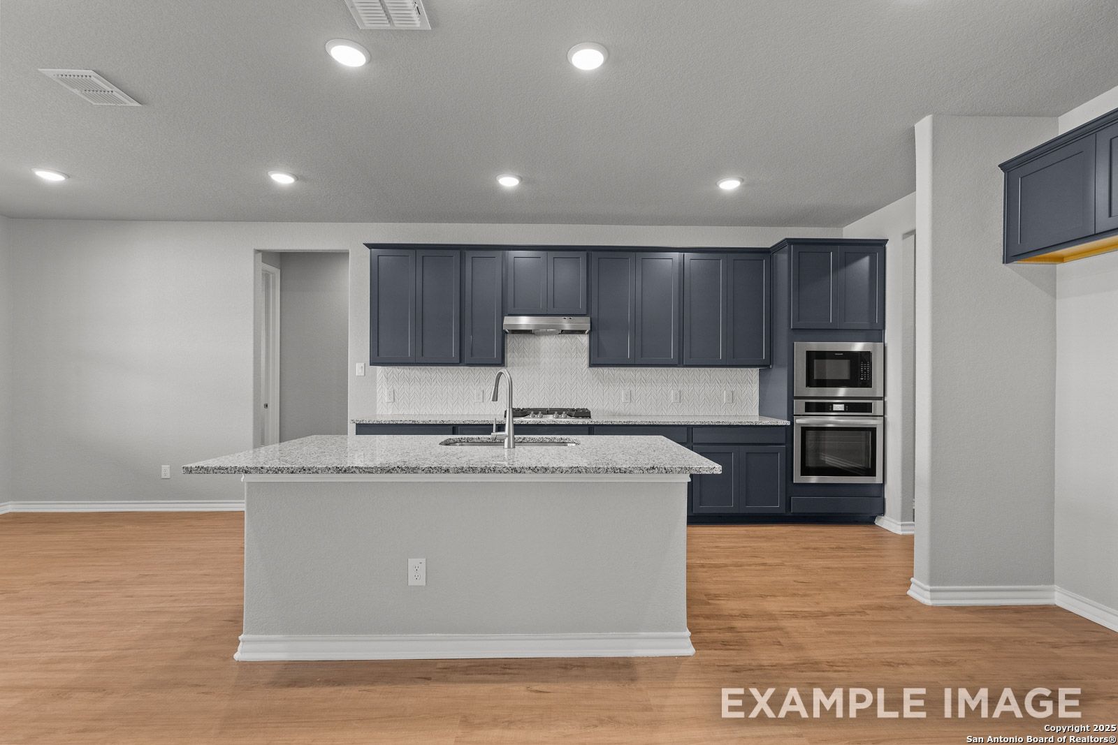 Modern kitchen in The Oxford H featuring dark blue cabinets, granite island, and stainless steel appliances in Castroville, TX.