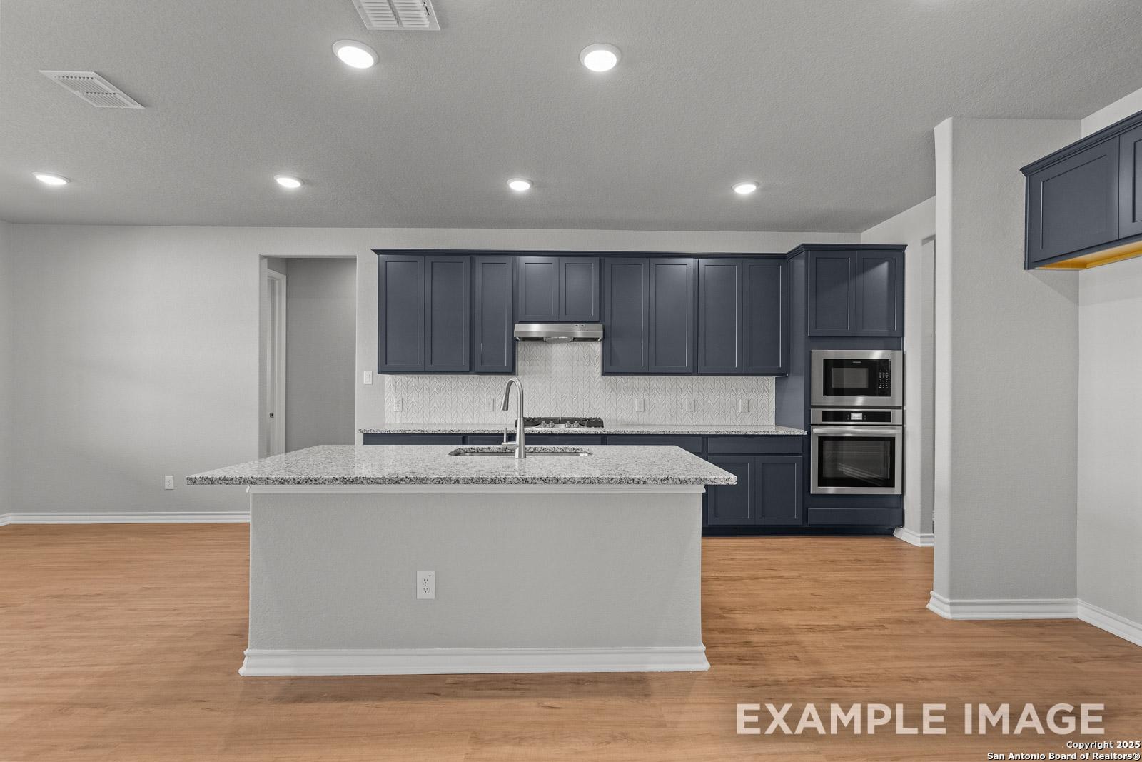 Modern kitchen in The Oxford H featuring dark blue cabinets, granite island, and stainless steel appliances in Castroville, TX.