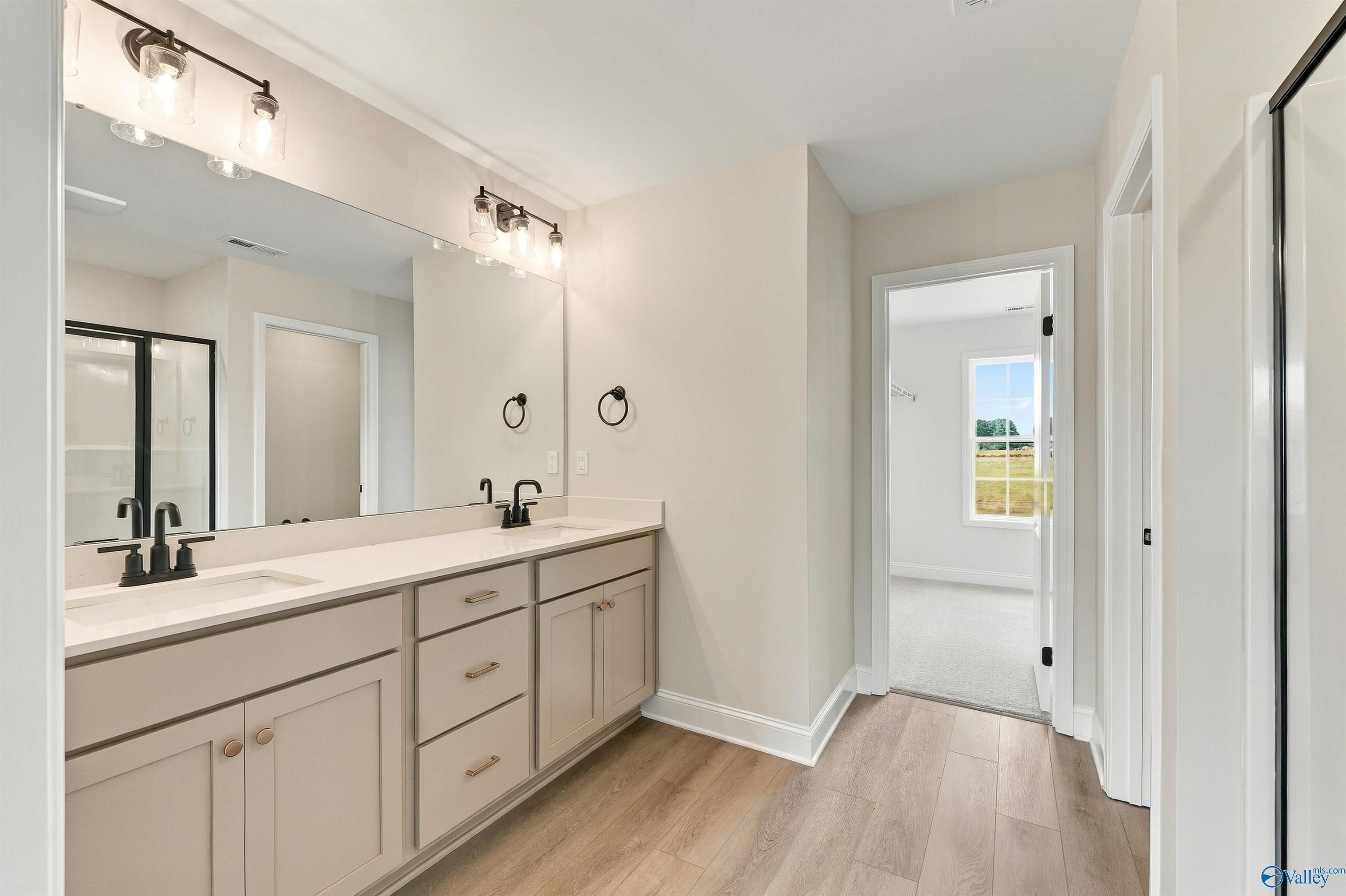 Double vanity bathroom with beige cabinets, matte black fixtures, and wide mirror in Davidson Homes The Shelby A, Athens, Alabama