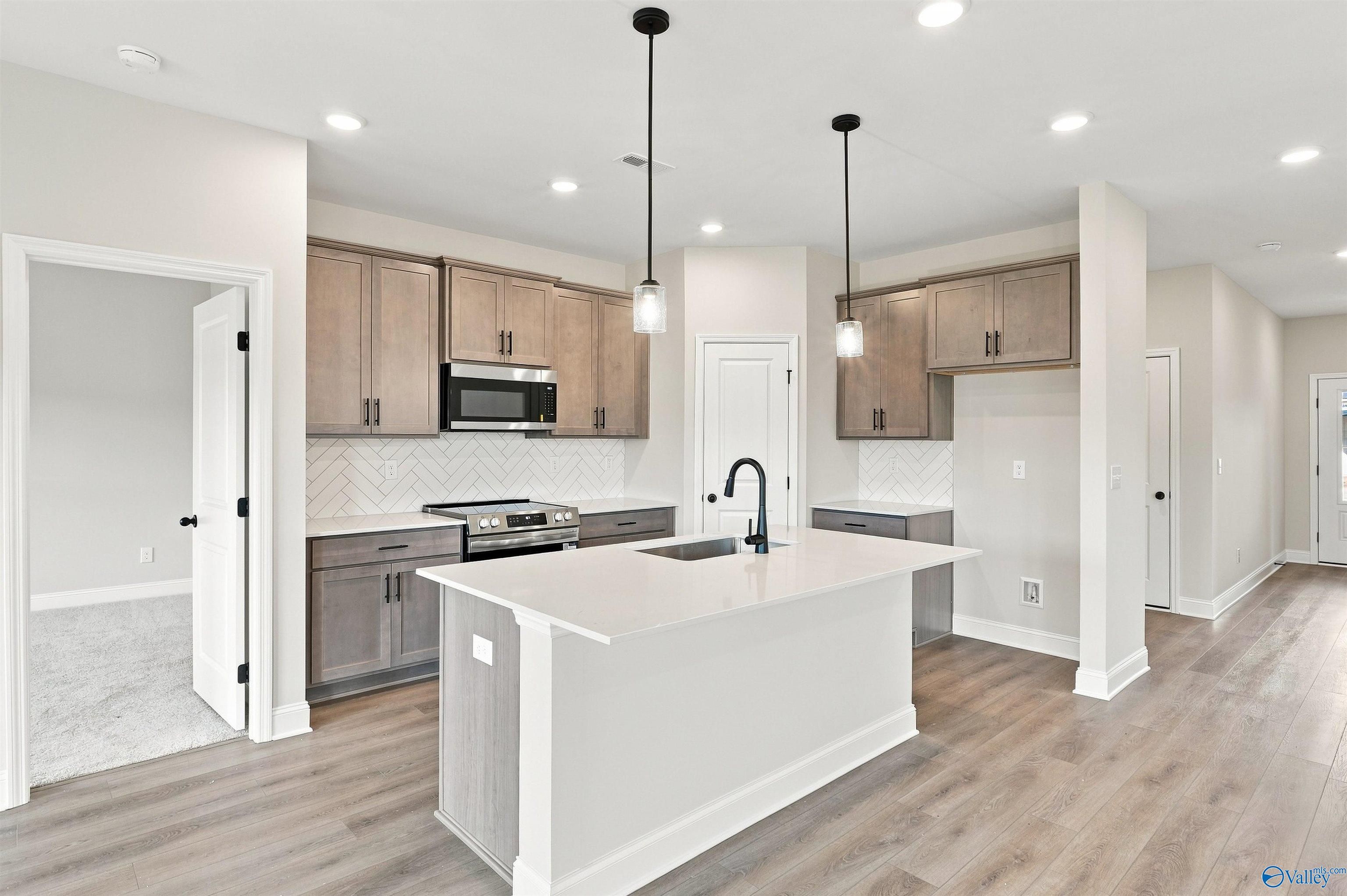 Modern kitchen with island, herringbone backsplash, and wood floors in Davidson Homes Franklin C plan, The Meadows, Athens, Alabama