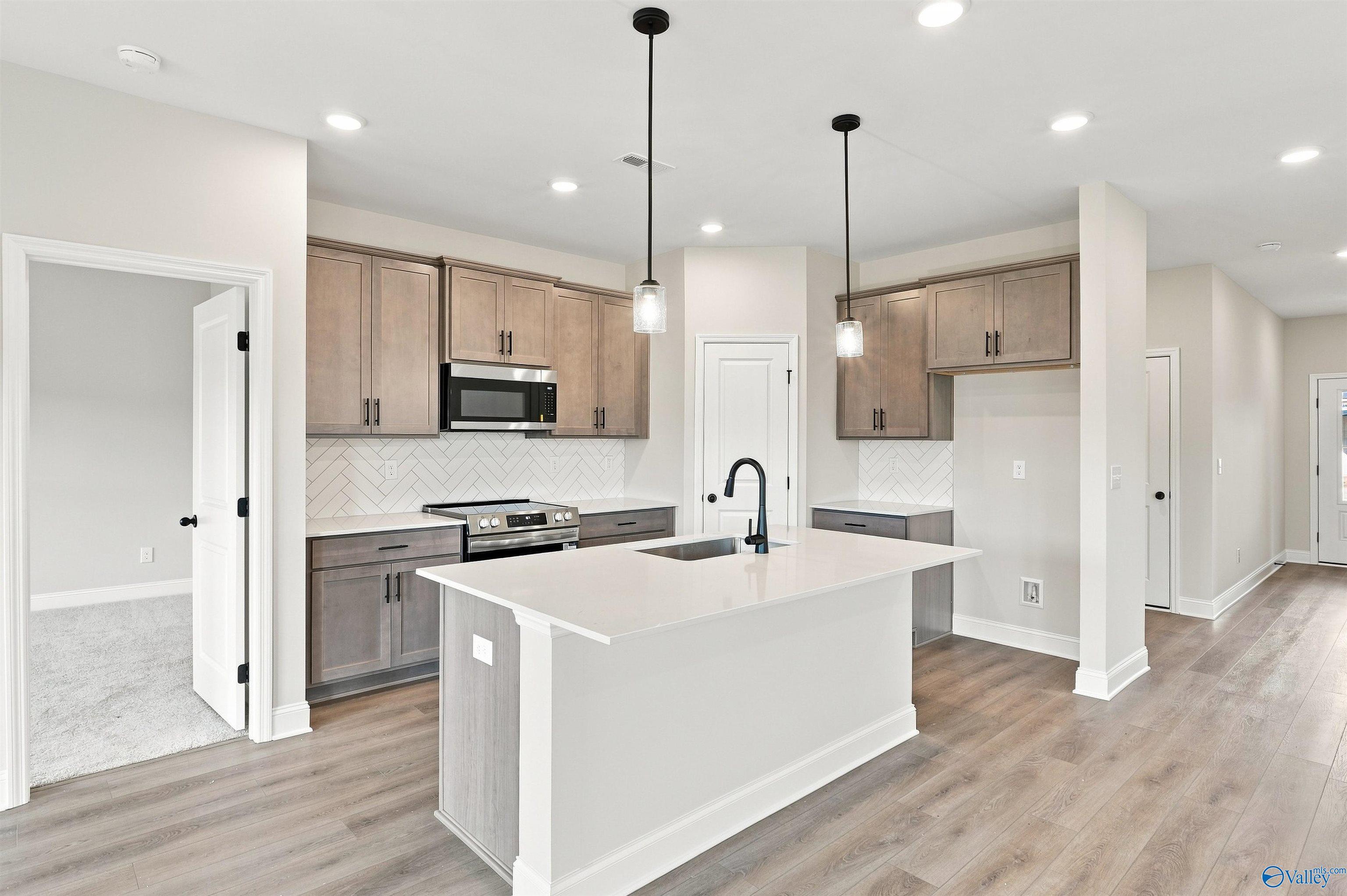 Modern kitchen with island, herringbone backsplash, and wood floors in Davidson Homes Franklin C plan, The Meadows, Athens, Alabama