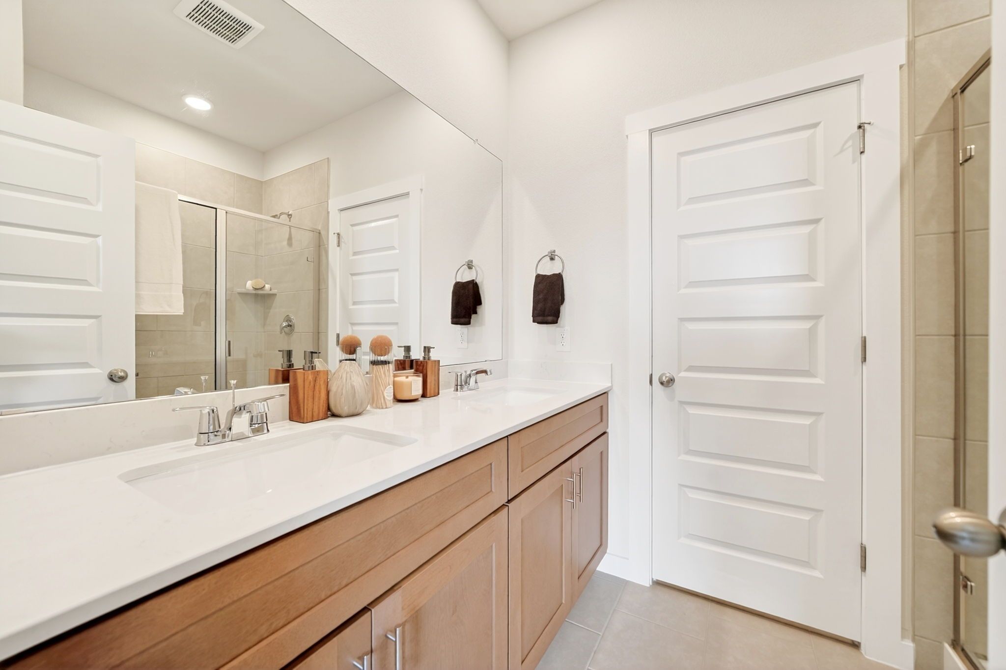 Elegant primary bathroom at Heartland in Texas with quartz double vanity, wood cabinets, large mirror, and tiled walk-in shower