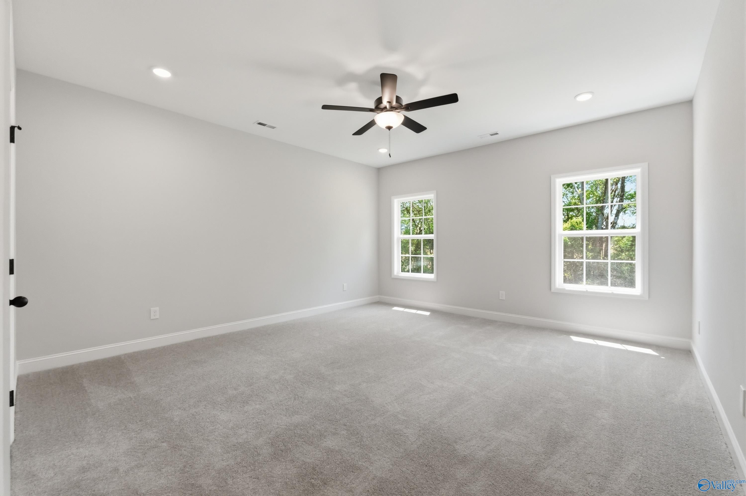 Spacious bedroom with ceiling fan, gray carpet, and tree-view windows in Davidson Homes The Rockford B, Athens, Alabama