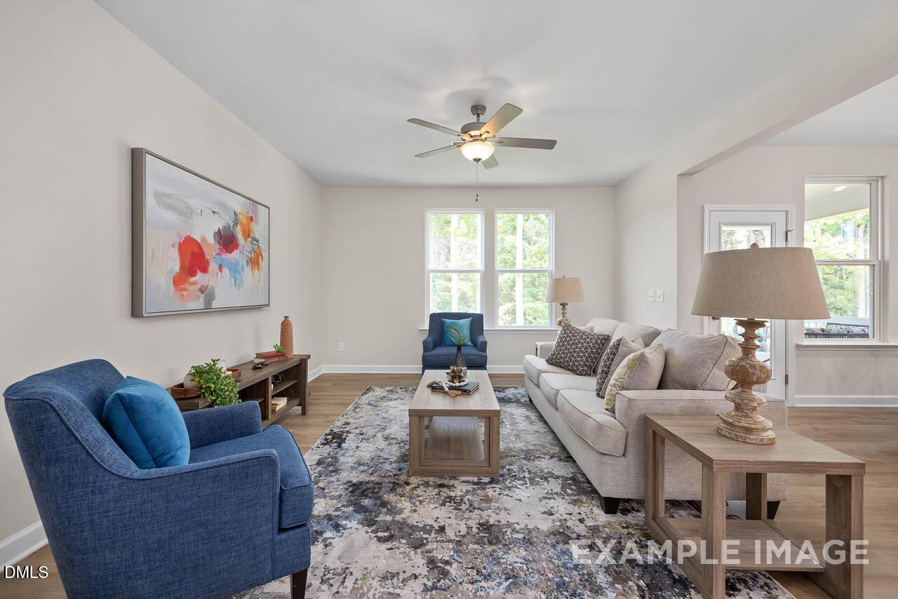 Cozy living room with blue accent chair, cream sofa, wooden tables, abstract wall art, and ceiling fan in Davidson Homes The Willow D, Lillington, NC
