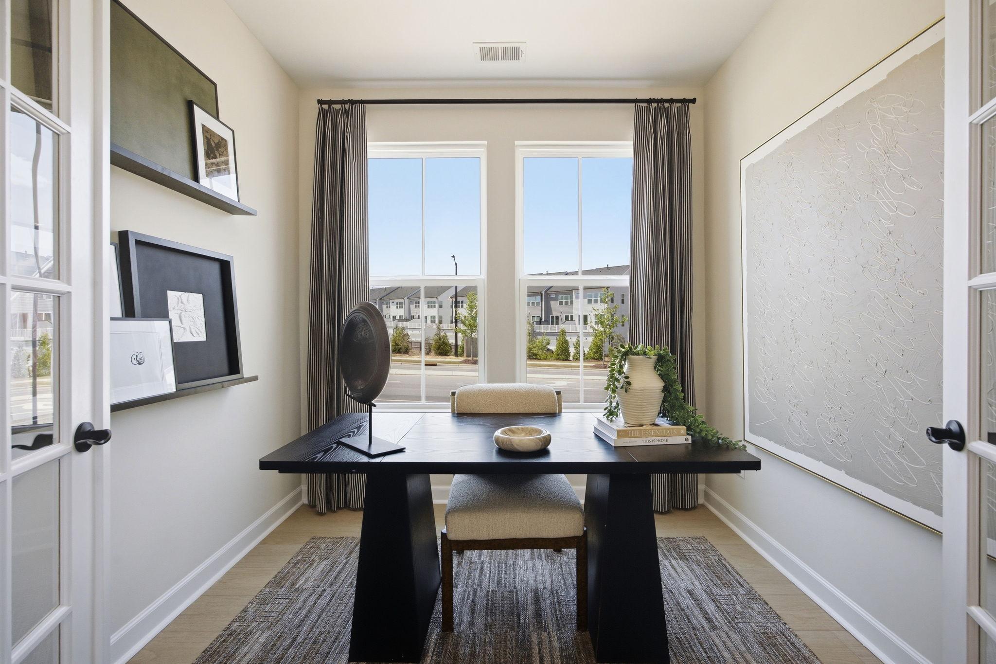 Modern home office at Forestville Yard in Knightdale, NC by Davidson Homes featuring black desk and French door entry.