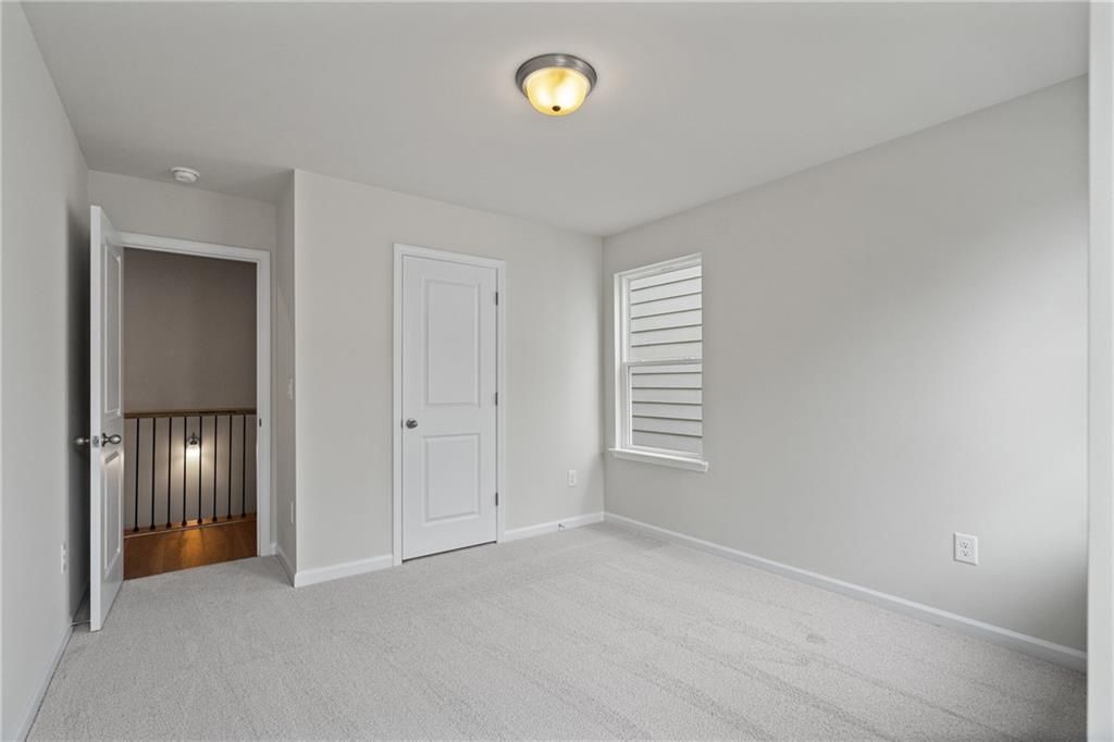 Bright upstairs bedroom with gray walls, carpet floor, and balcony railing in Davidson Homes The Marion B, Kennesaw, GA