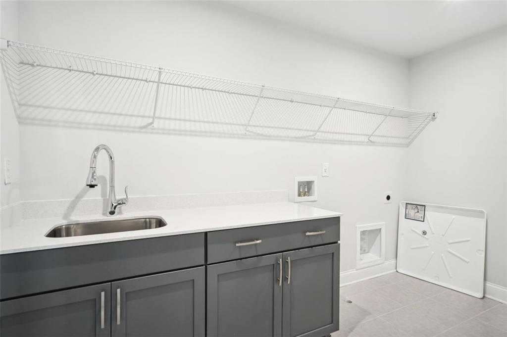 Modern laundry room with white quartz countertop, stainless sink, gray shaker cabinets, and wire shelving in Davidson Homes Hickory C, Hoschton, GA