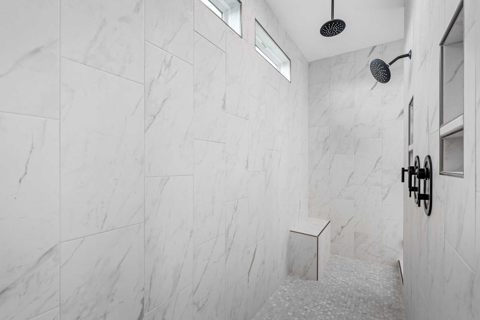 Elegant walk-in shower with white marble tiles, dual rain showerheads, black fixtures, and built-in bench in Davidson Homes The Alston A, Murfreesboro