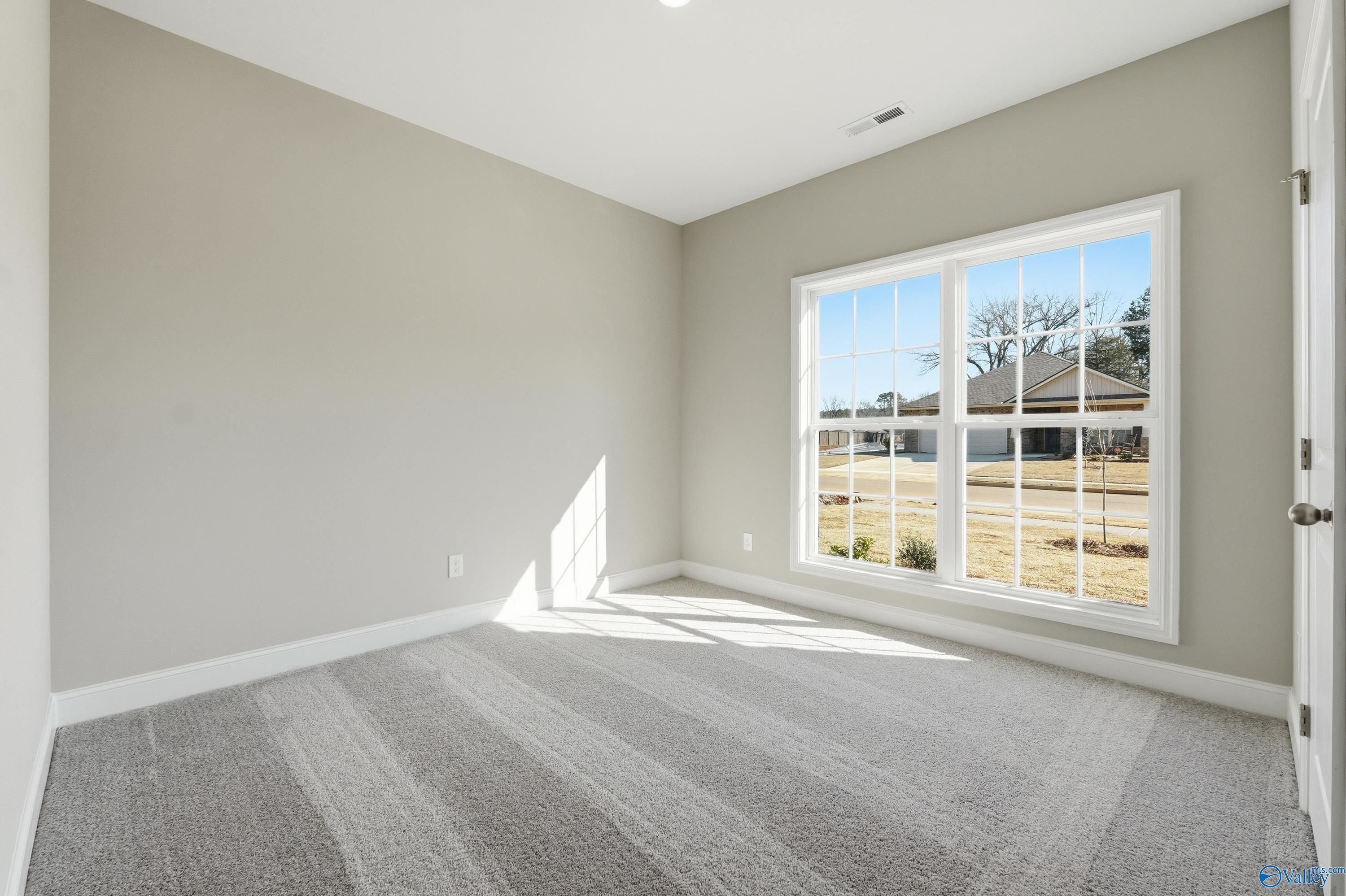 Bright empty bedroom with neutral gray walls, plush carpet, and large window overlooking yard in Davidson Homes Franklin C, New Market AL