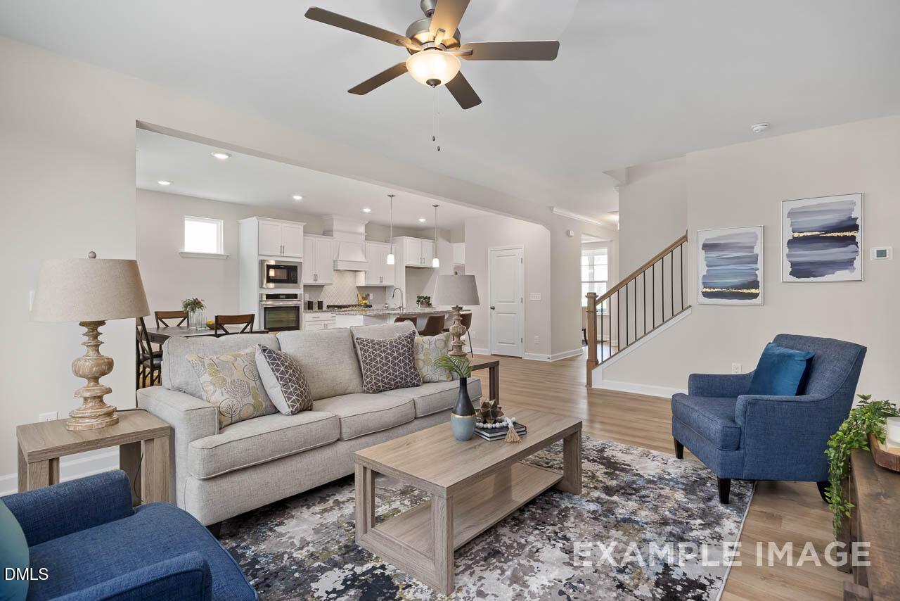 Cozy open-concept living room with beige sofa, blue armchair, ceiling fan, and kitchen view in The Willow D, Lillington, NC