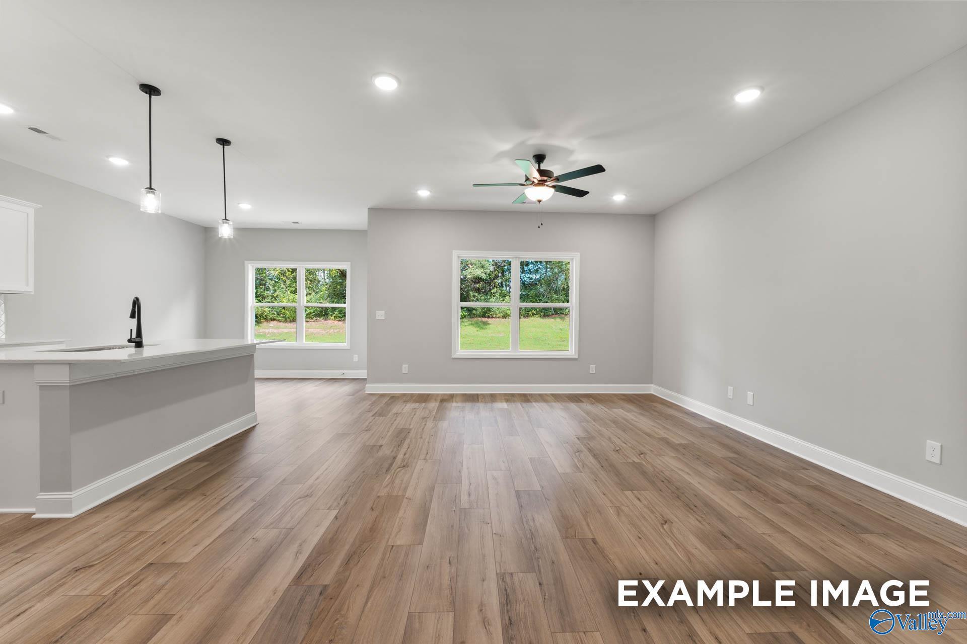 Open-concept kitchen and living area with gray walls, wood floors, large windows, and ceiling fan in The Asheville C by Davidson Homes, Hazel Green, AL